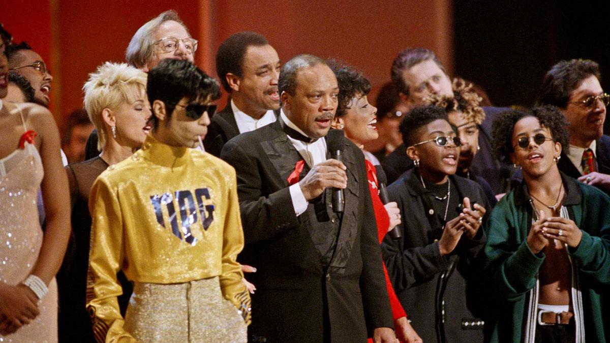 Prince, next to Quincy Jones, wearing gold pants and a shiny yellow shirt