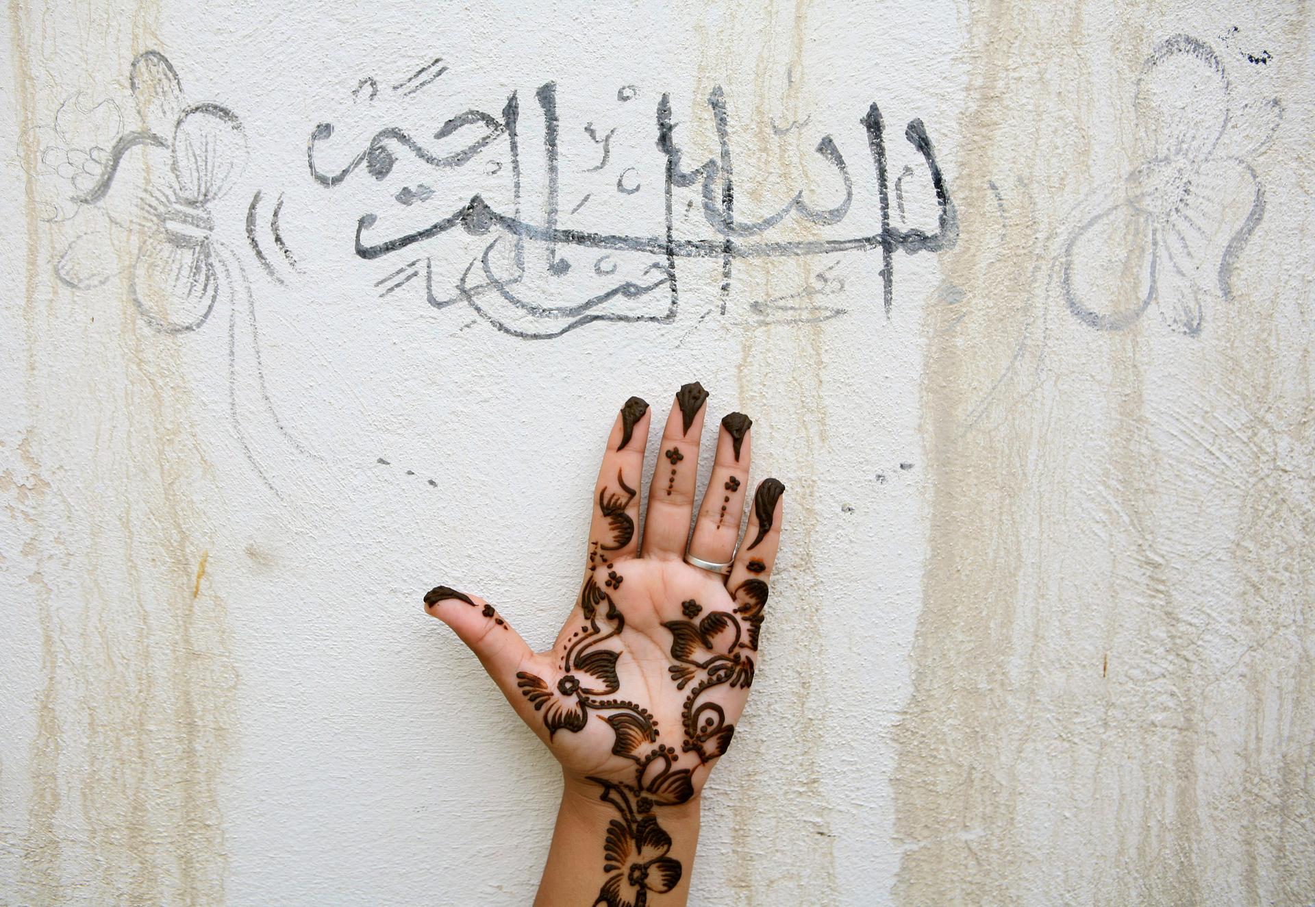 An Iranian woman holds up her hand, painted with henna, under a religious sentence as she prepares for a wedding ceremony in the city of Qeshm on Qeshm Island at the Persian Gulf, November 1, 2006. The sentence reads, "In the name of Allah, the Beneficent