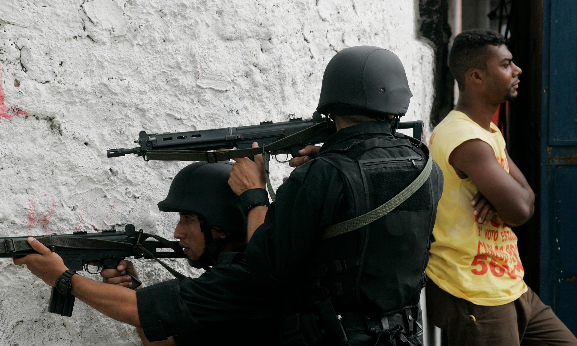 Brazilian elite police officers take aim near a resident of the Complexo do Alemao slum as they carry out raids to control the escalating violence between drug gangs, in Rio de Janeiro in 2007.