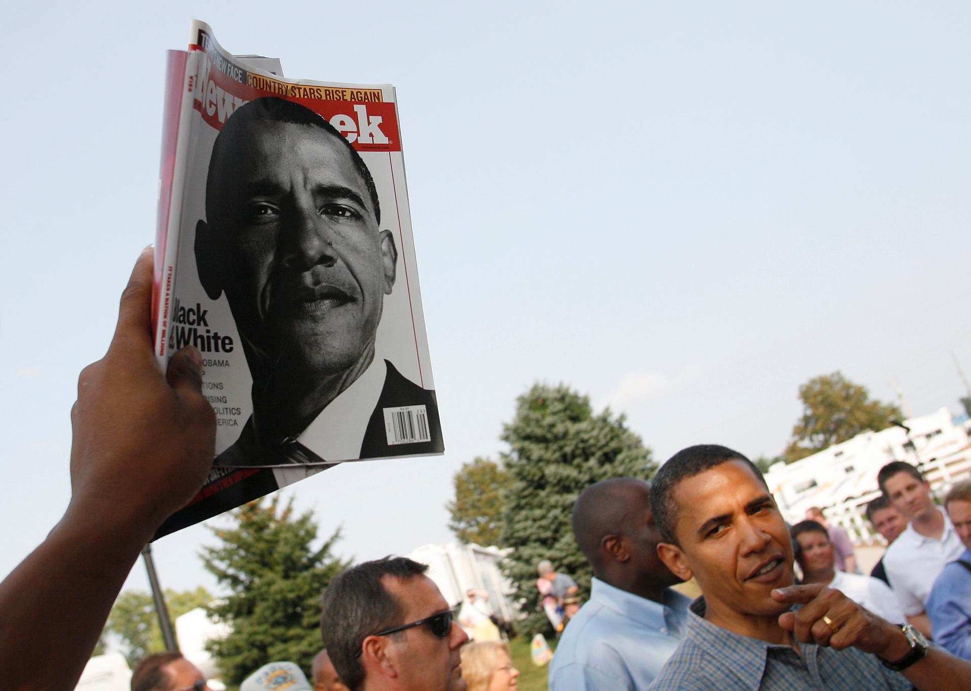 hand holds up magazine with Barack Obama on cover, with Obama nearby