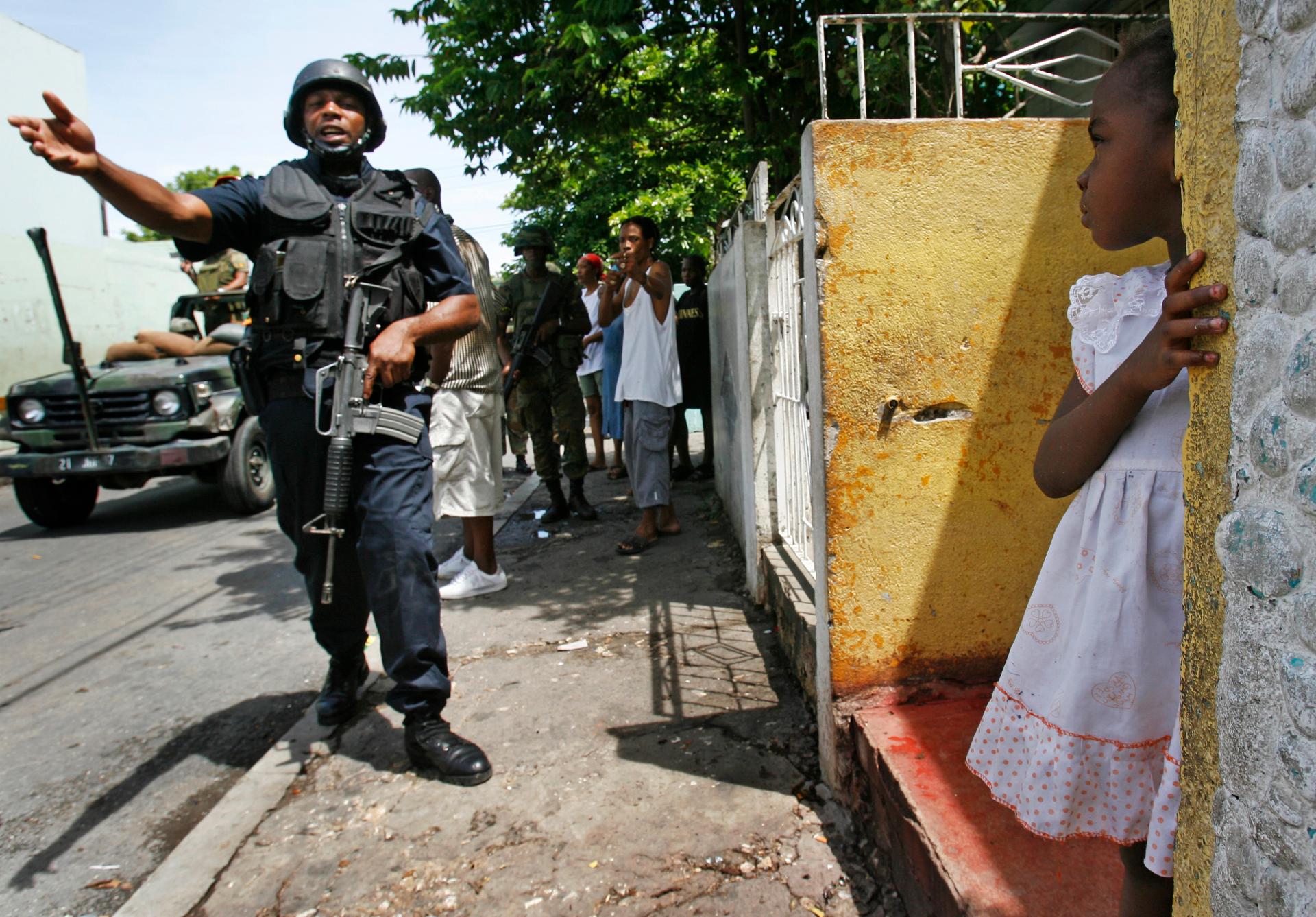 A police officer patrols the street as a little girl watches from her doorstep in the Tivoli Gardens neighborhood of Kingston, Jamaica, on May 27, 2010.
