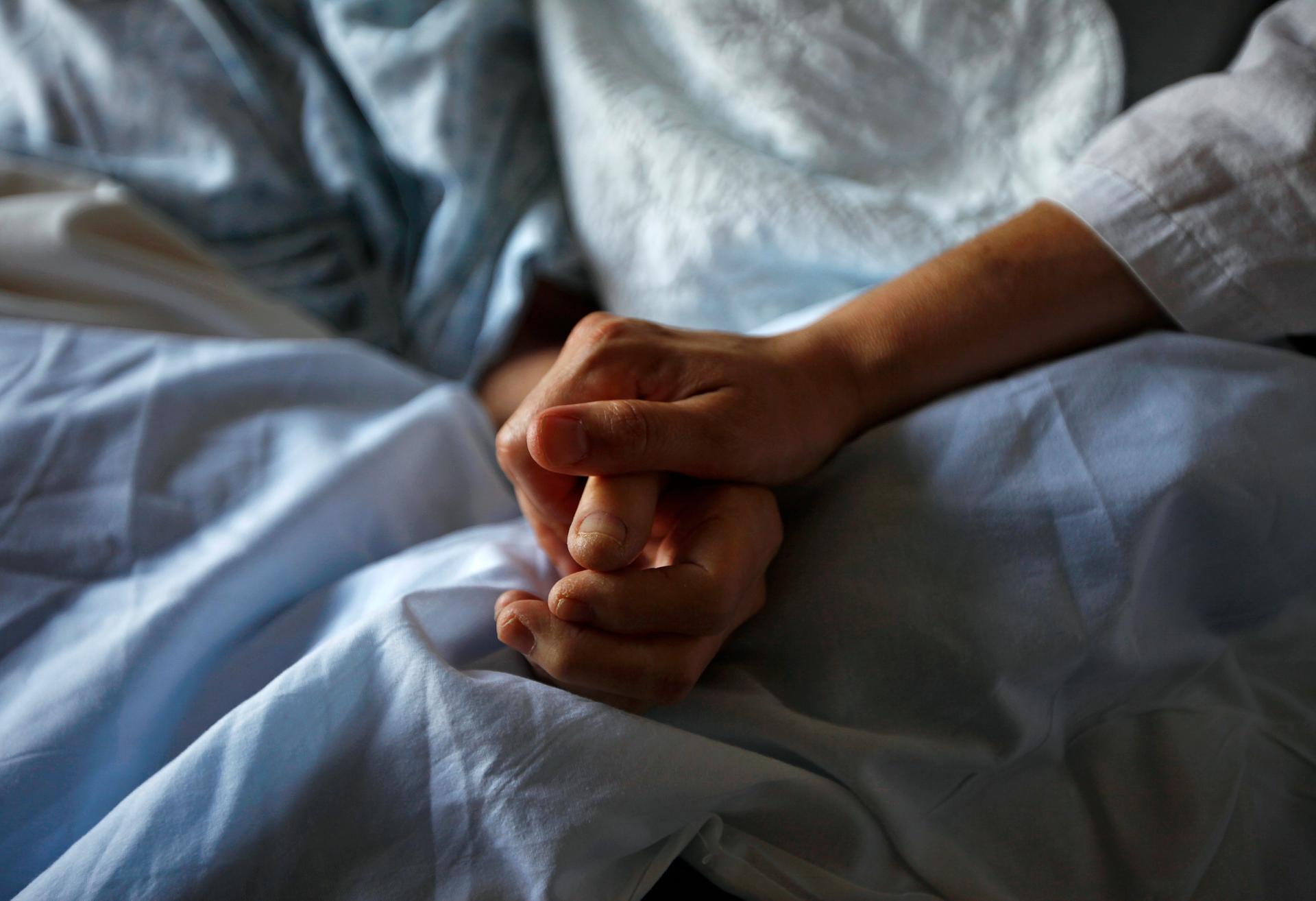A woman holds the hand of her mother who is dying from cancer during her final hours at a palliative care hospital in Winnipeg, Canada