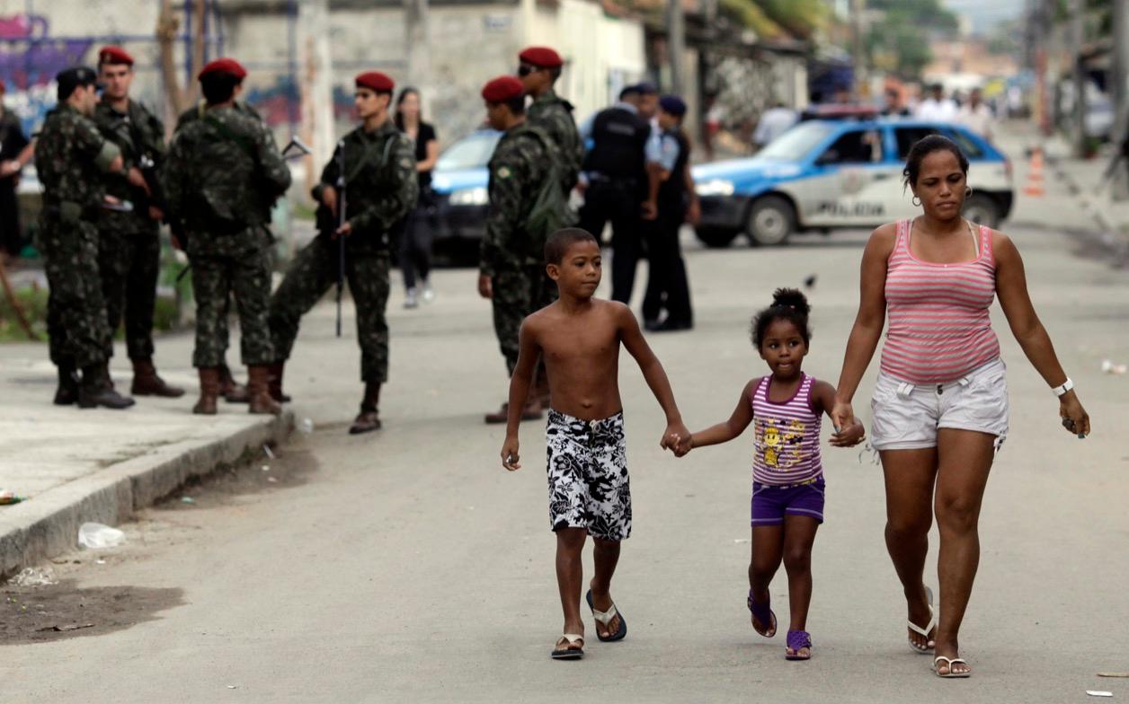 Residents walk by security forces in Cidade de Deus, Rio