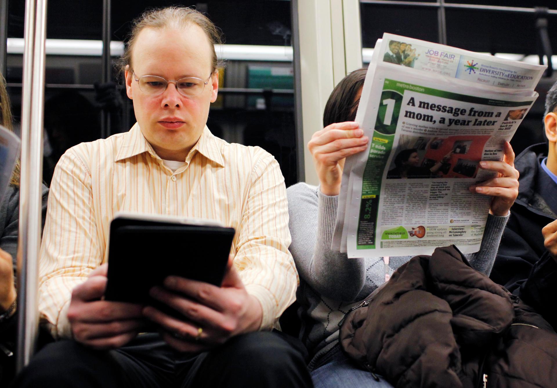 A commuter reads on a Kindle e-reader while riding the subway in Cambridge, Mass. Neuroscience says the way his brain treats reading on the Kindle is different than the way the brain processes the newspaper next to him.