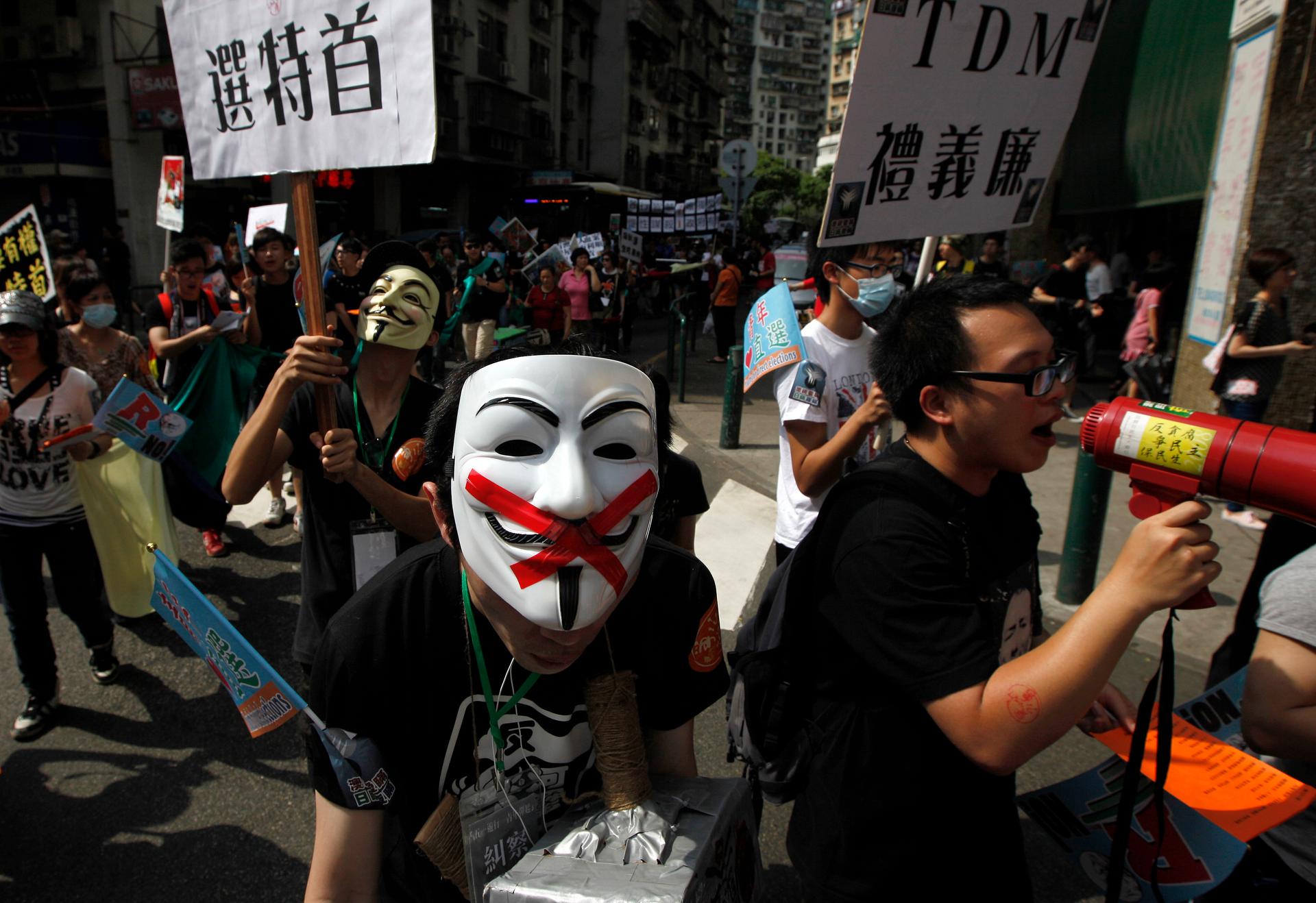 Pro-democracy demonstrators wearing Anonymous masks hold placards during a protest march demanding universal suffrage for Macau on May 1, 2012. The placard reads "Vote for Chief Executive." 