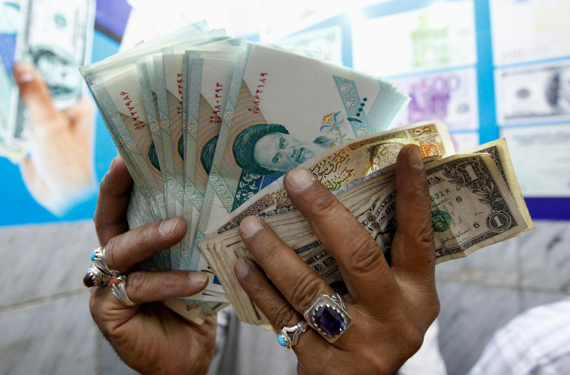 A woman holds up Iranian rials and dollars in a market