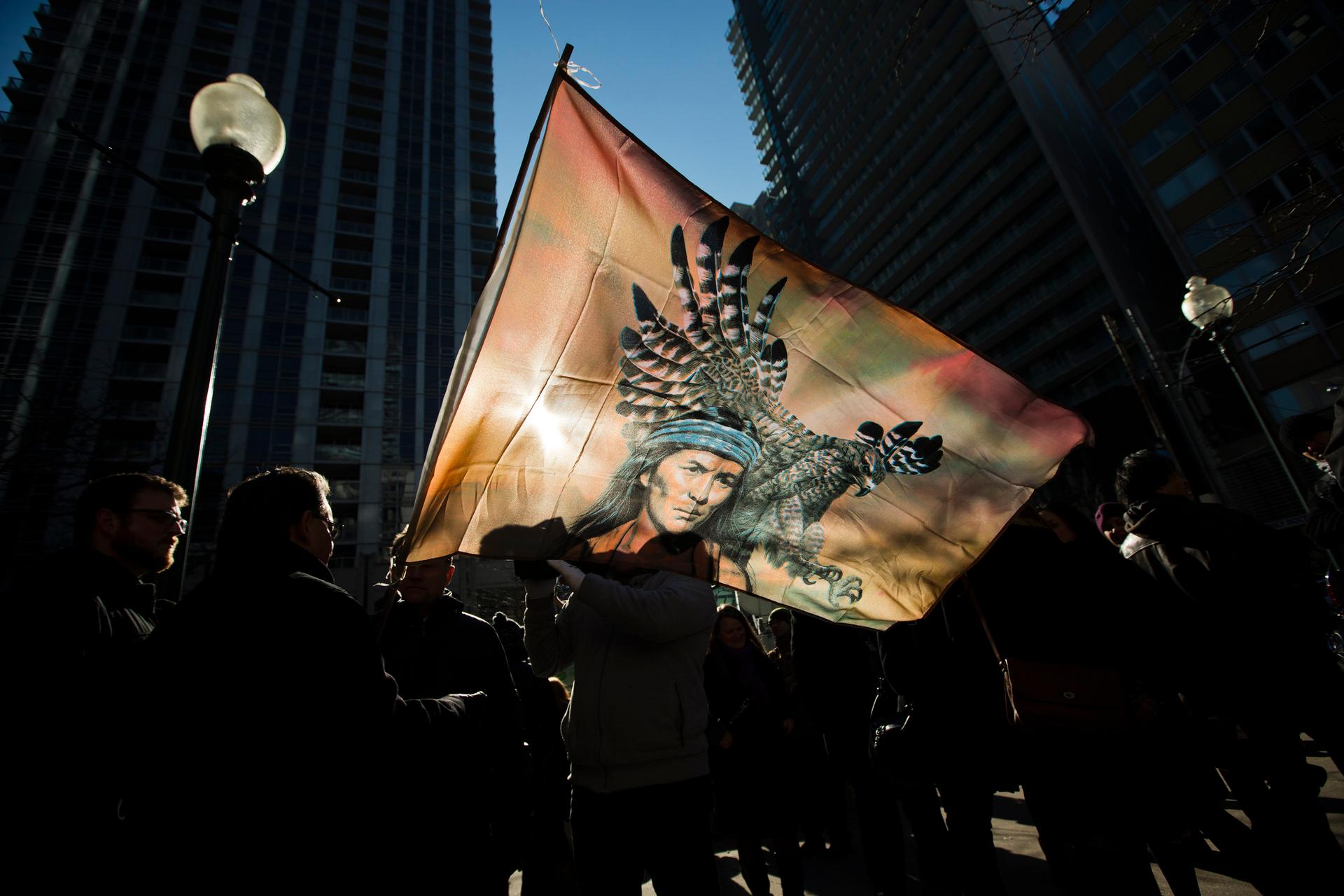 First Nations protesters are silhouetted behind a flag in a "Idle No More" demonstration in Toronto.