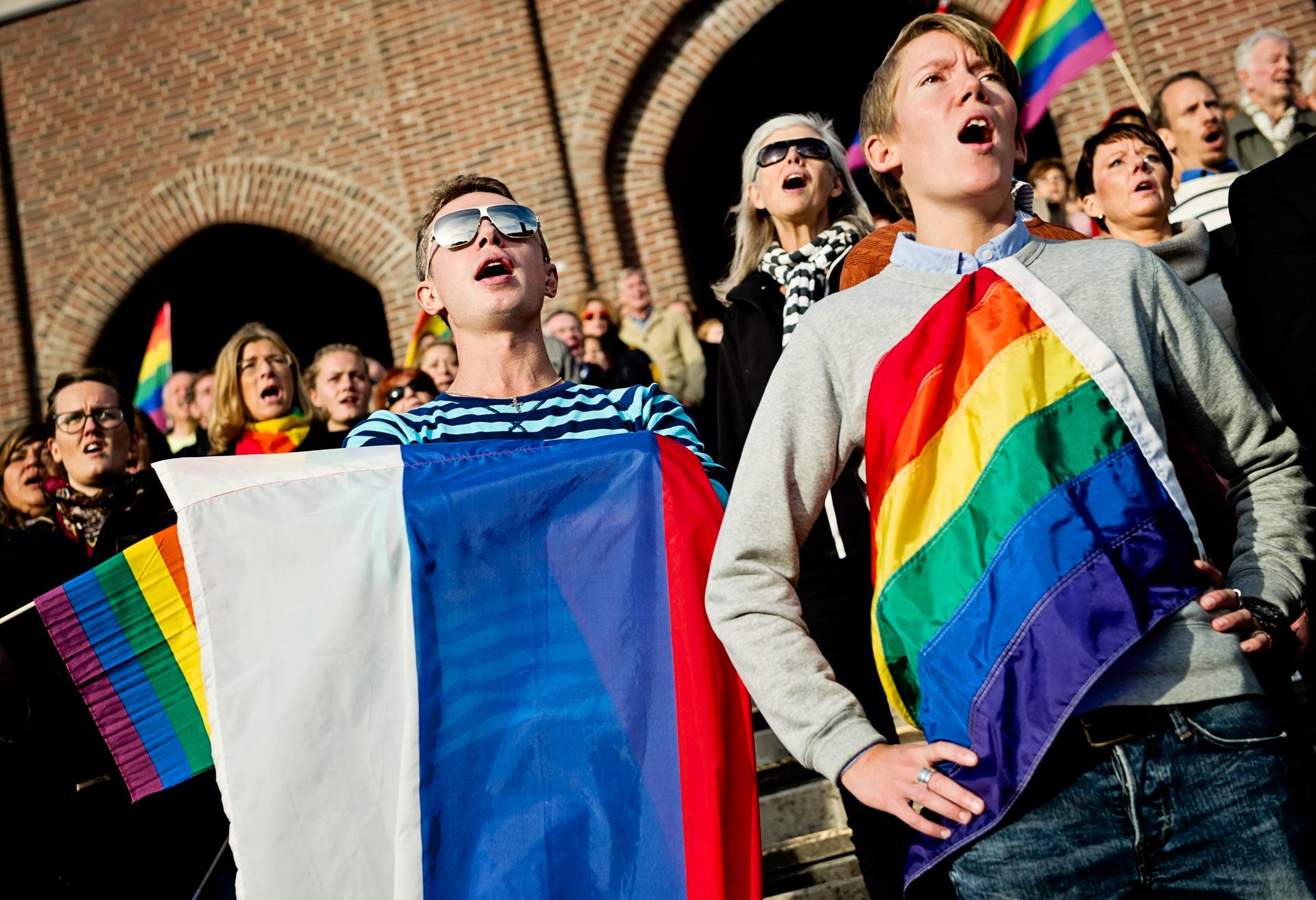 People sing the Russian national anthem while raising rainbow flags and a Russian flag  at the Stockholm Olympic Stadium 