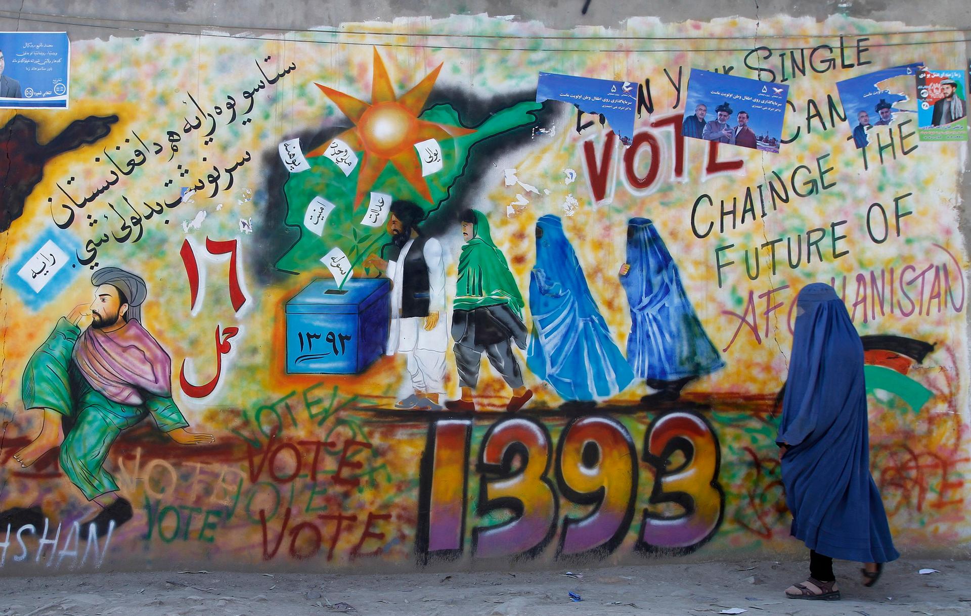 A woman in Kandahar walks past a wall with graffiti encouraging people to vote in Sunday's elections. 