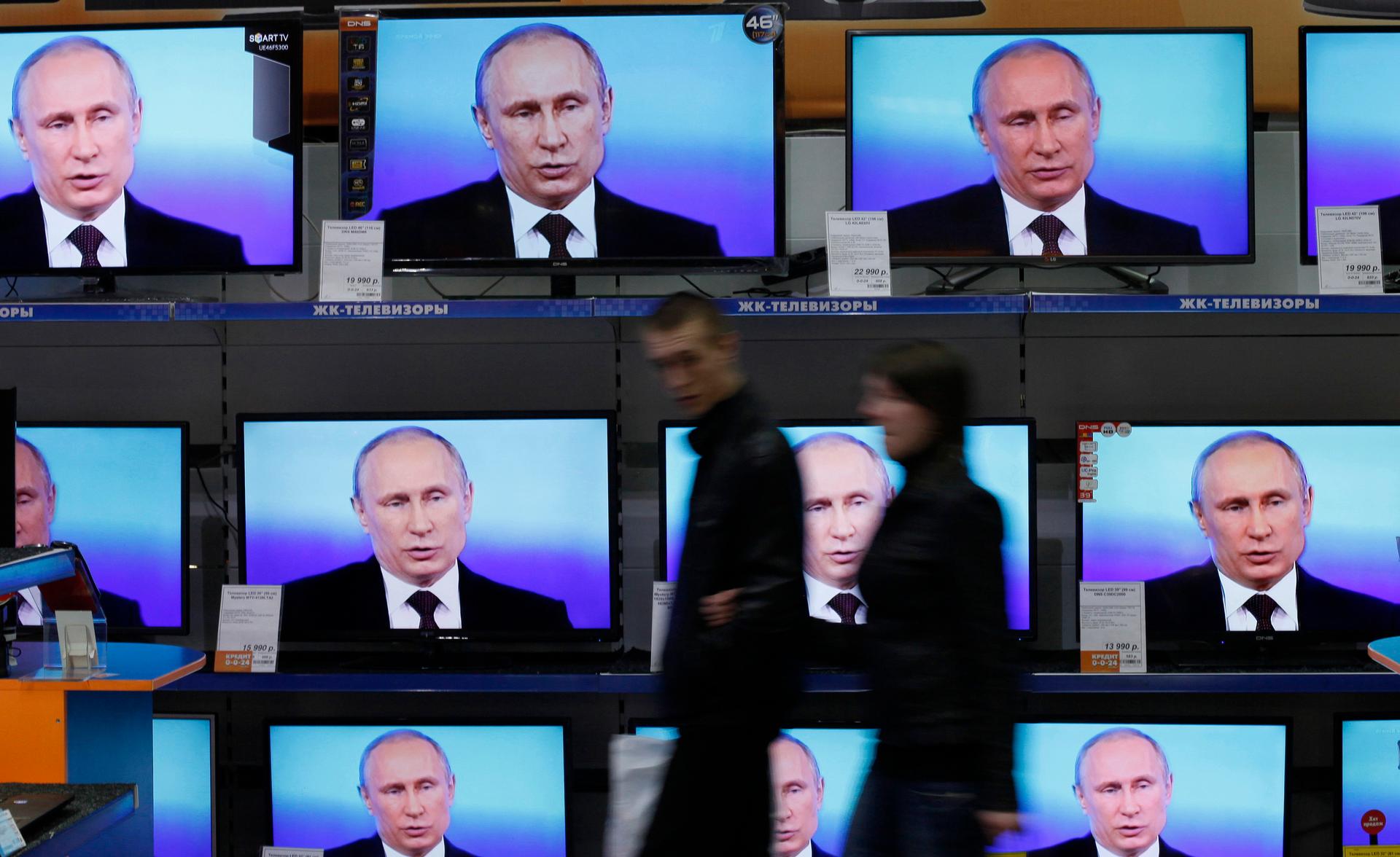 Visitors walk past TV sets during Russian President Vladimir Putin's live broadcast nationwide phone-in at the DNS electronic shop in Russia's Siberian city of Krasnoyarsk.