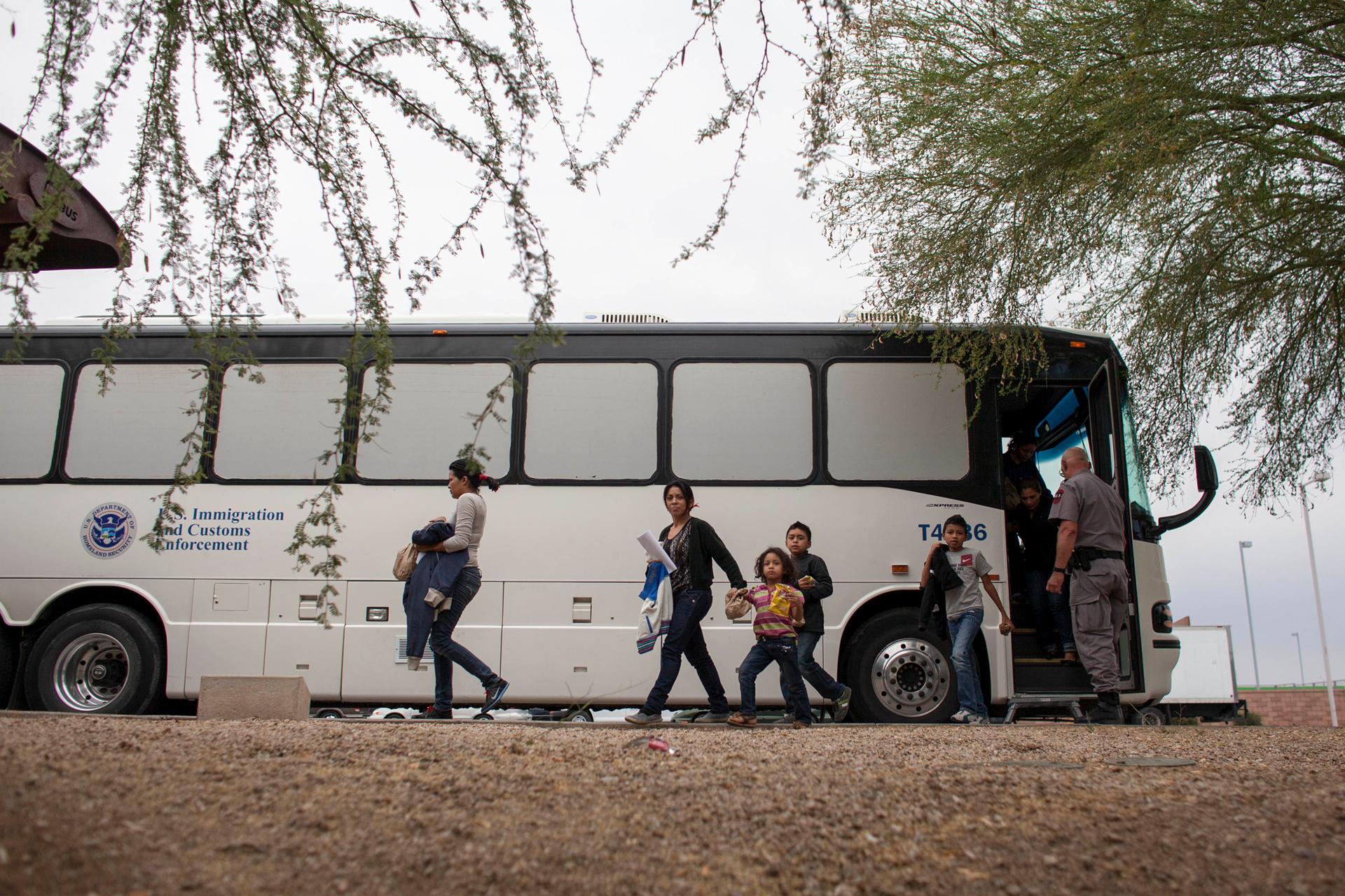 Women and children disembark from a bus marked with the insignia of the ICE