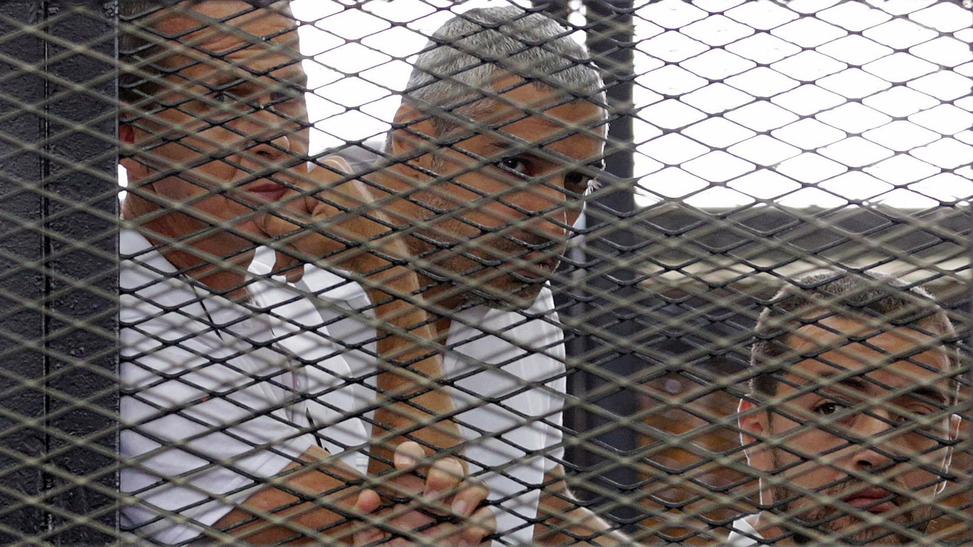 Al Jazeera journalists (L-R) Peter Greste, Mohammed Fahmy and Baher Mohamed stand behind bars at a court in Cairo last summer.
