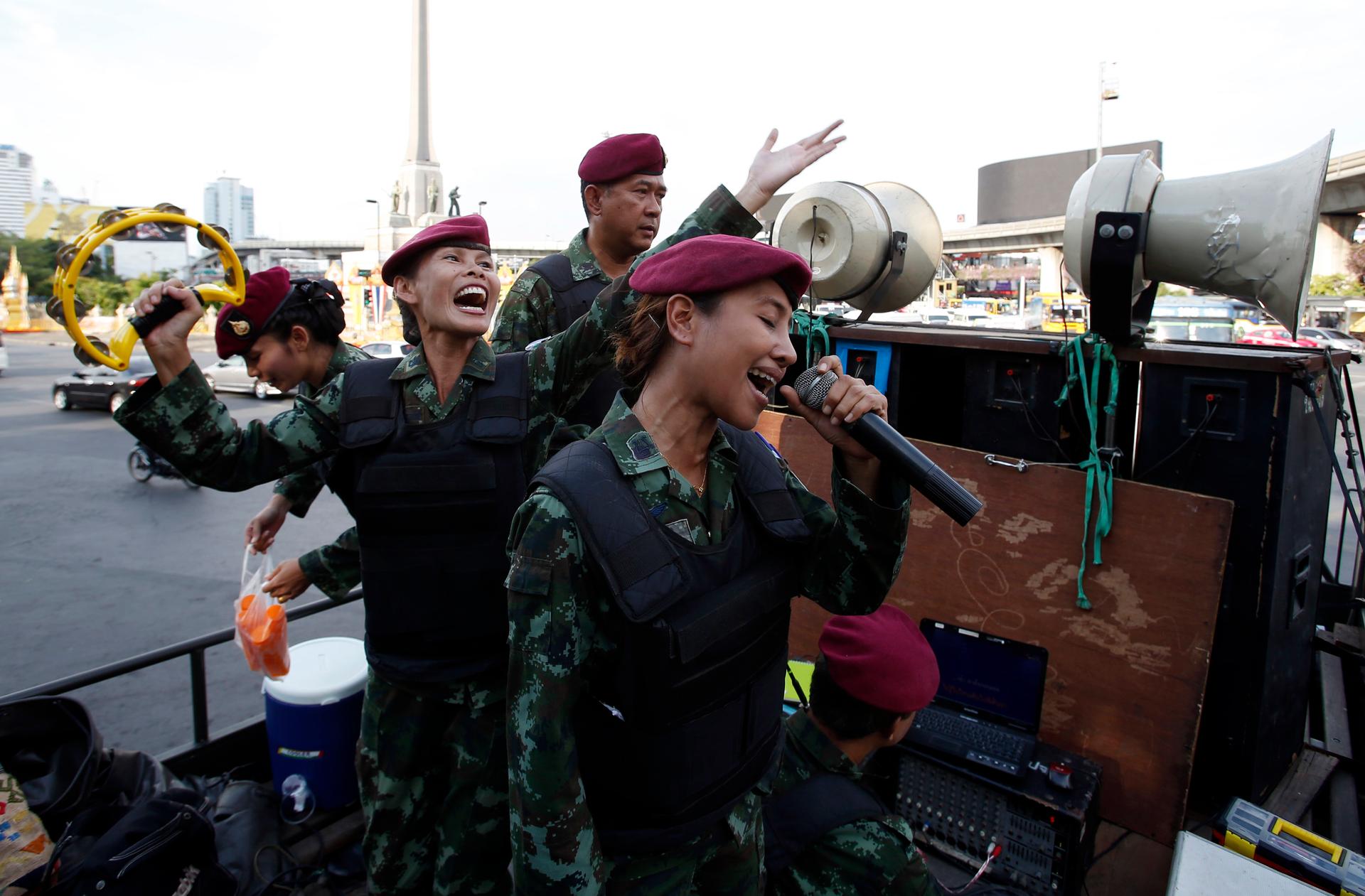 Female Thai soldiers sing patriotic songs on a military truck as soldiers and police take positions to prevent demonstrations against military rule