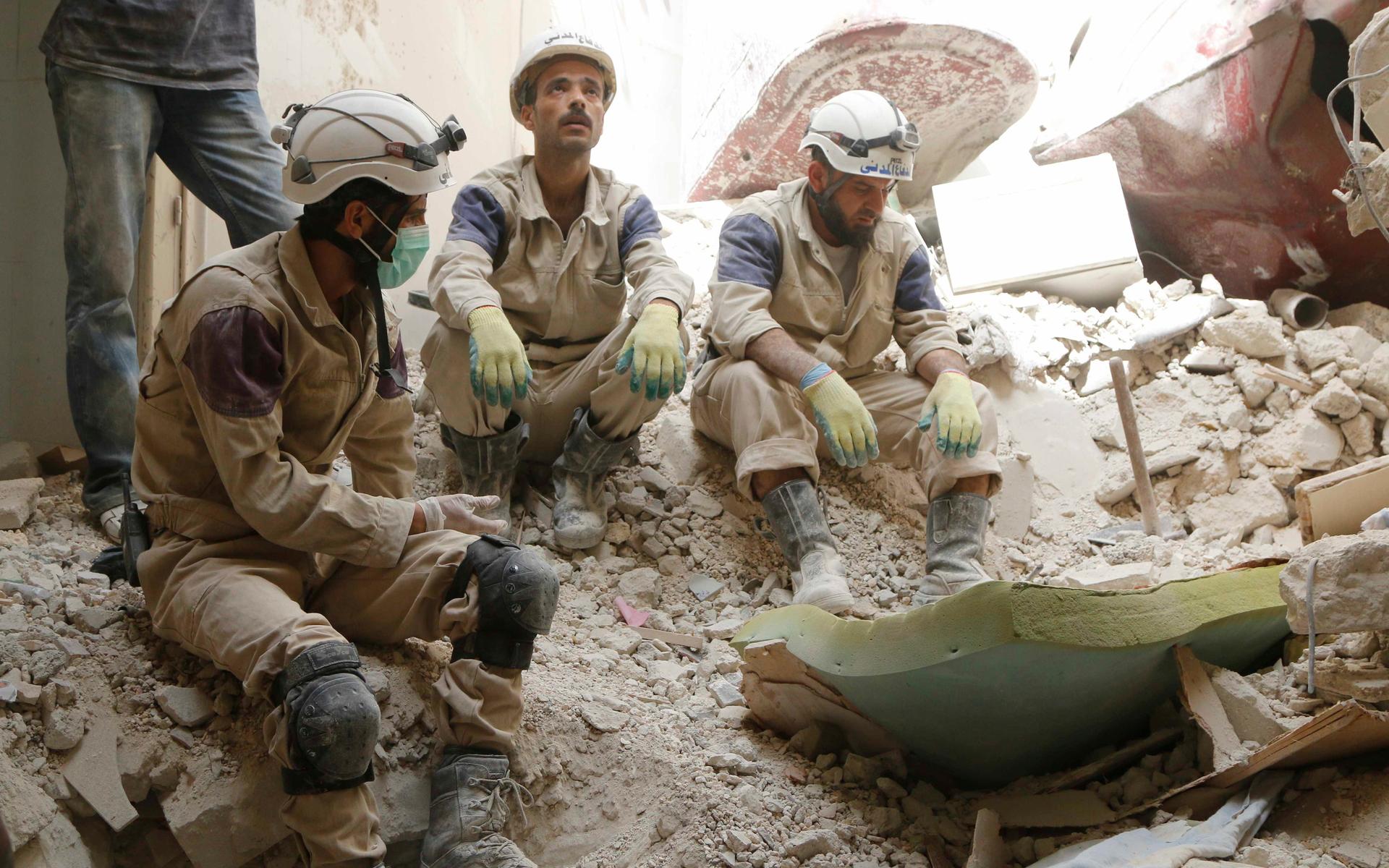 Three men sit in rubble in white helmets