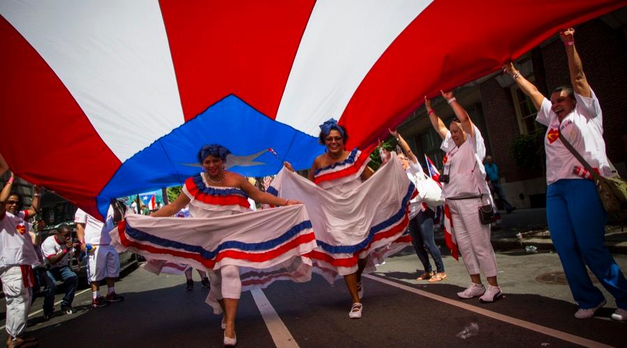 Women run under a Puerto Rican flag before the National Puerto Rican Day Parade on Fifth Avenue in Manhattan