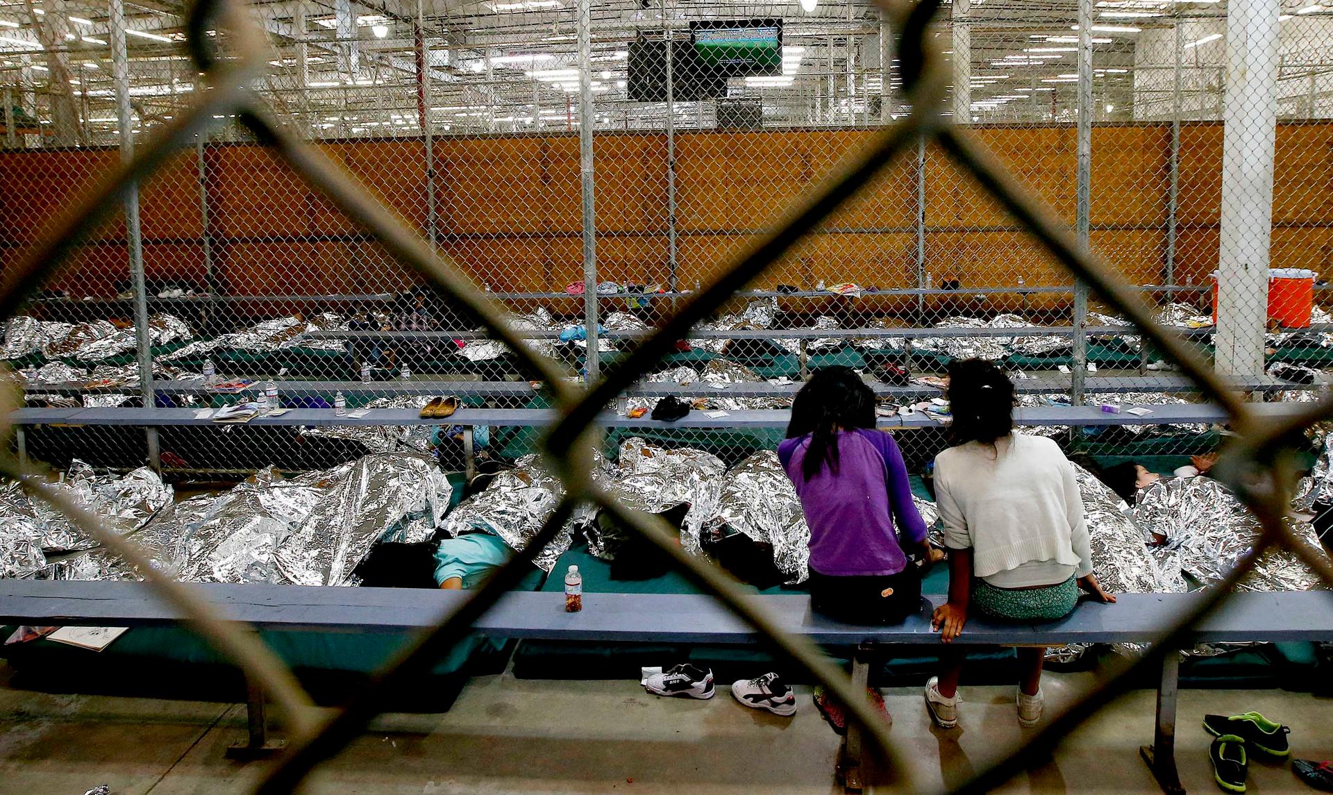 Two young girls watch television in a holding area where hundreds of mostly Central American immigrant children were being processed and held at the US Customs and Border Protection Nogales Placement Center in Nogales, Arizona, June 18, 2014. 