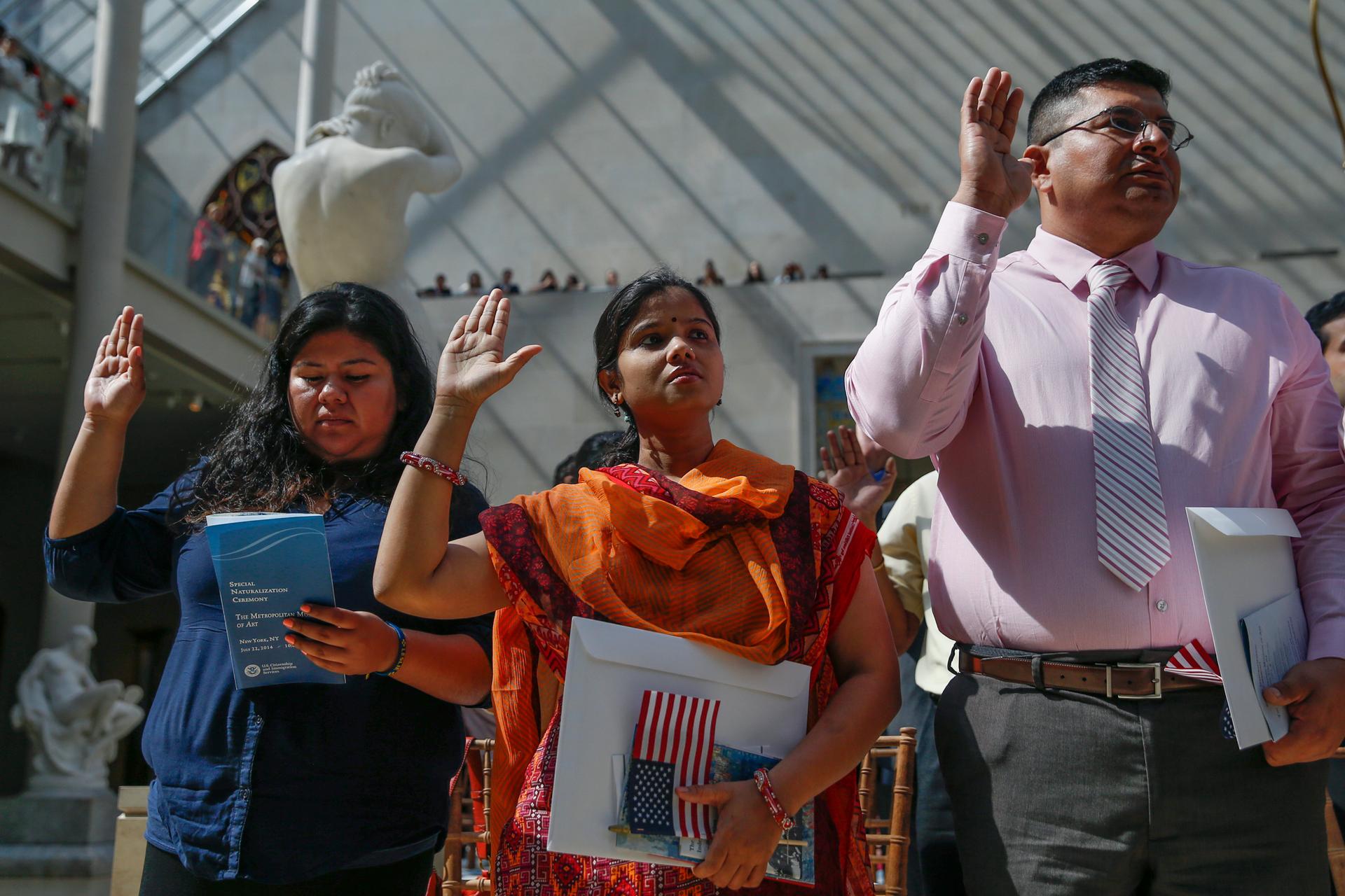 New American citizens (L to R) Leslie Tapia, from Mexico, Sanzida Khanam, from Bangladesh and Pablo Espinales, from Ecuador, raise their hands for the Pledge of Allegiance during a naturalization ceremony at The Metropolitan Museum of Art in New York on J