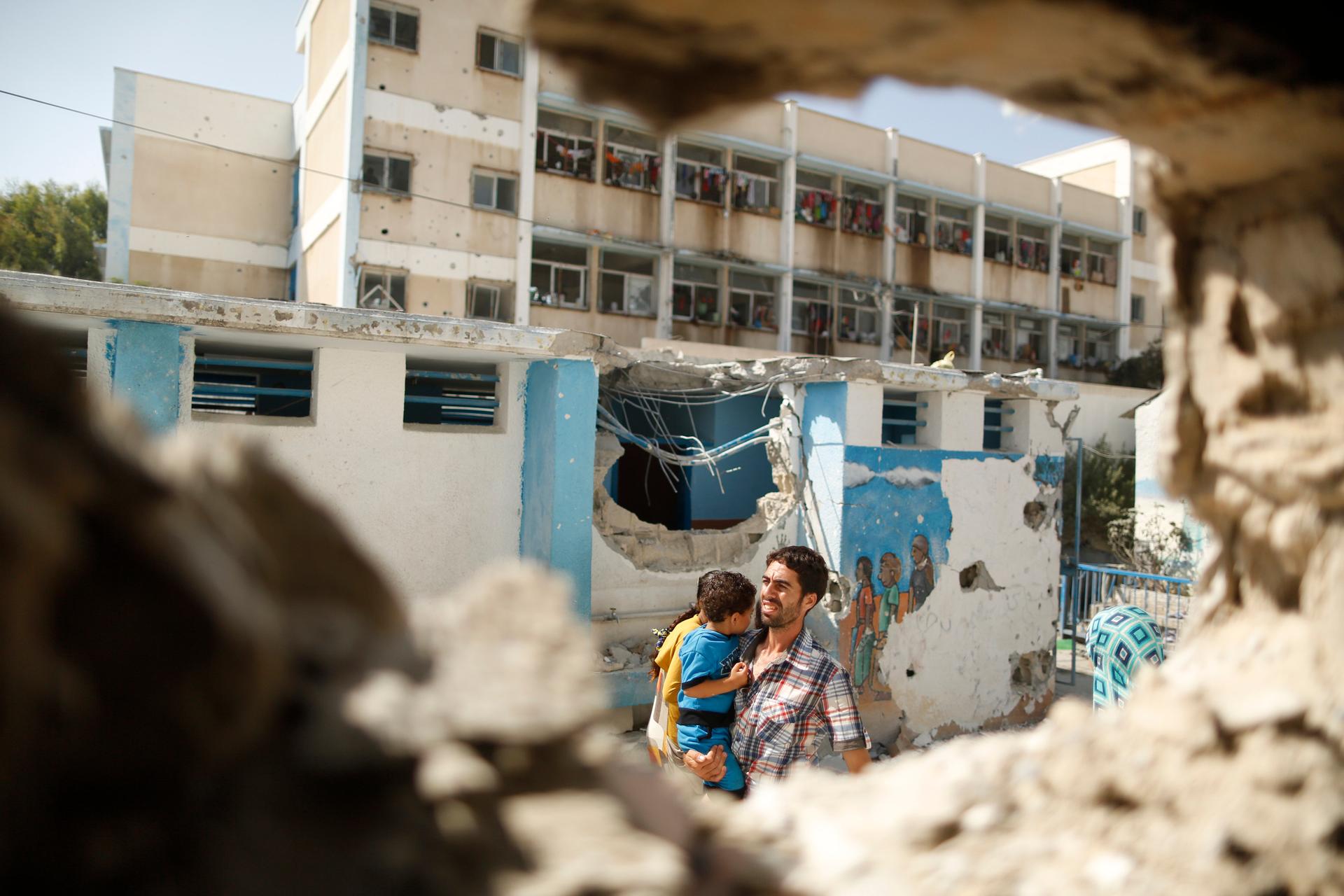 A Palestinian man, pictured through a damaged classroom, carries a boy as he walks at a United Nations-run school in the Jebaliya refugee camp in the northern Gaza Strip on July 30, 2014. Witnesses say the school, which is sheltering Palestinians displace