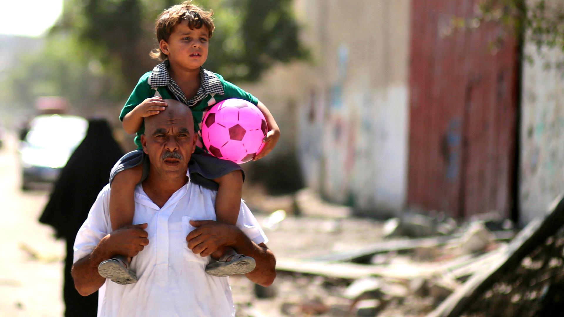 A Palestinian carries his son in the eastern Gaza City neighborhood of Shejaiya, which witnesses said was heavily hit by Israeli shelling and air strikes during an Israeli offensive. (August 1, 2014) 