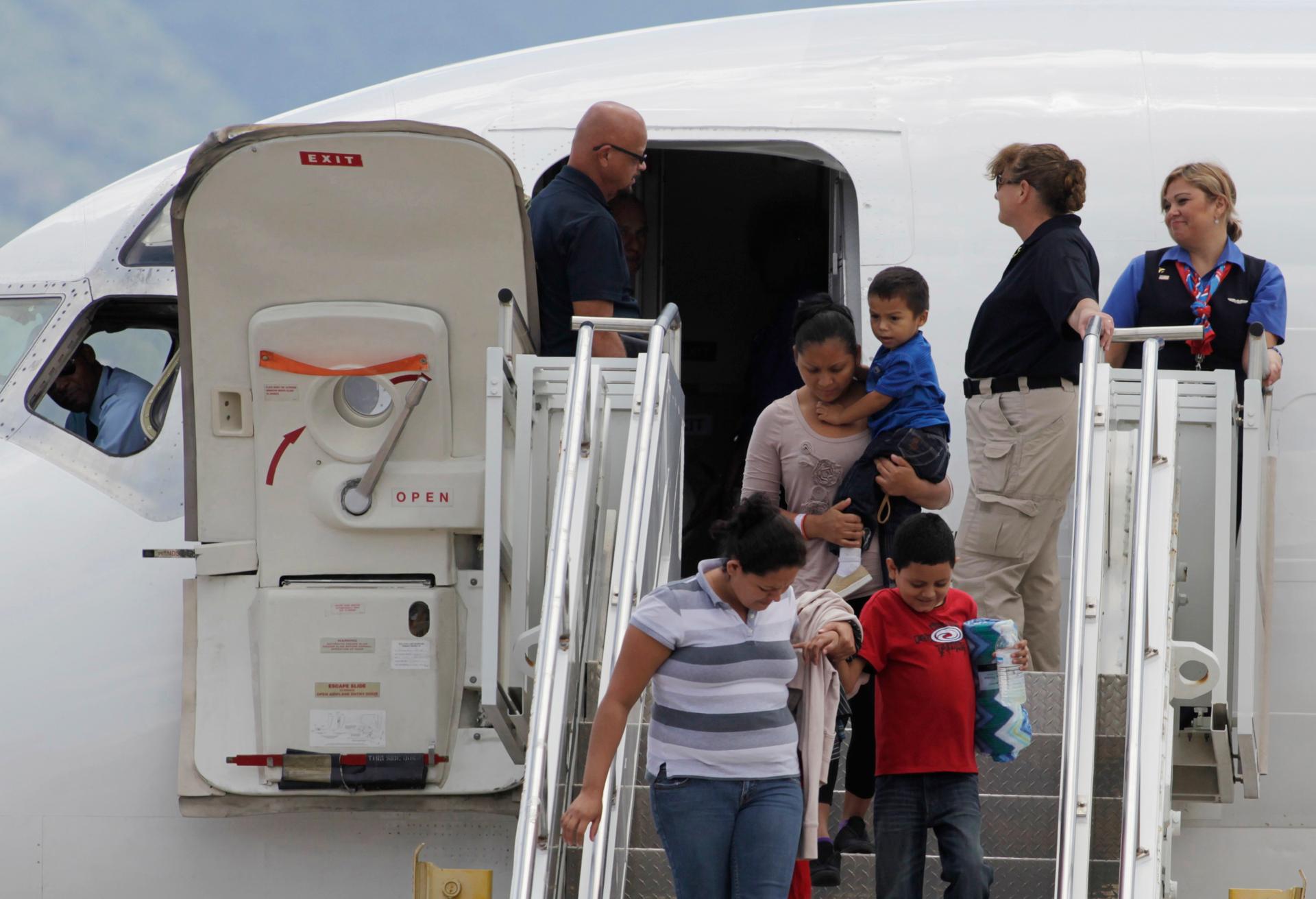 Women and children disembark from a plane, with agents around them