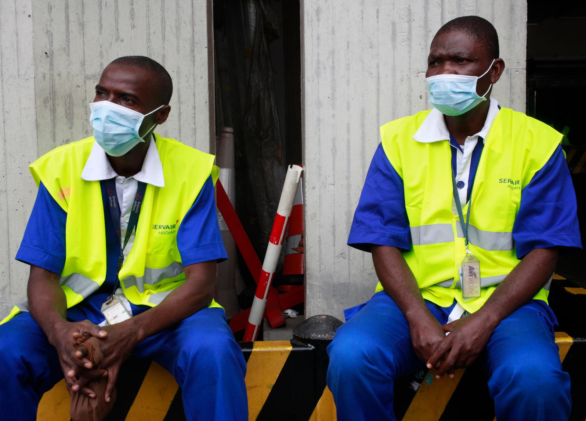 Workers wearing protective masks sit at the Felix Houphouet Boigny international airport in Abidjan. Ivory Coast on Monday banned air travelers from Liberia, Guinea and Sierra Leone, the three countries worst-hit by the Ebola outbreak.
