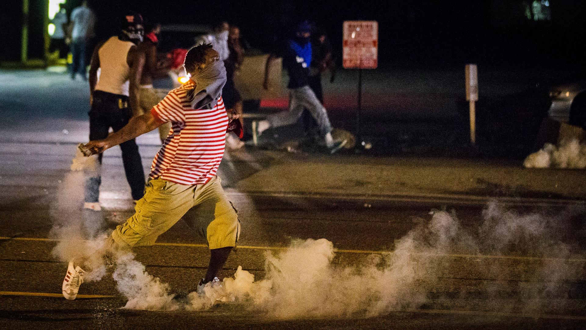 A protester picks up a gas canister to throw back towards the police after tear gas was fired at demonstrators during a protest in Ferguson, Missouri.