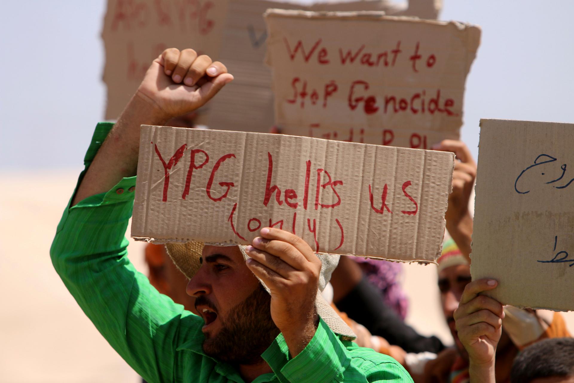 A refugee from the minority Yazidi sect carries a sign referring to the Kurdish People's Defence Units in Qamishli, northeastern Syria on August 17, 2014. Yazidis and Assyrians are two of the minority sects under assault from ISIS.