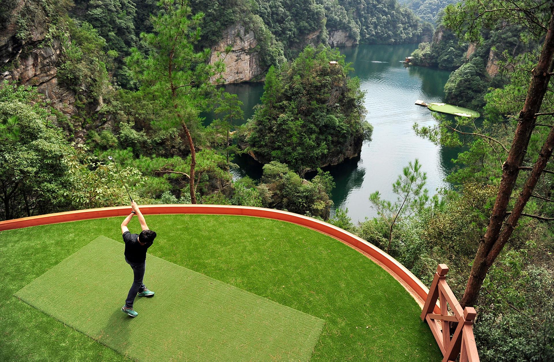 A staff member plays a shot towards a putting green on a lake from a tee ground on top of a hill, at Zhangjiajie, Hunan province September 23, 2014.