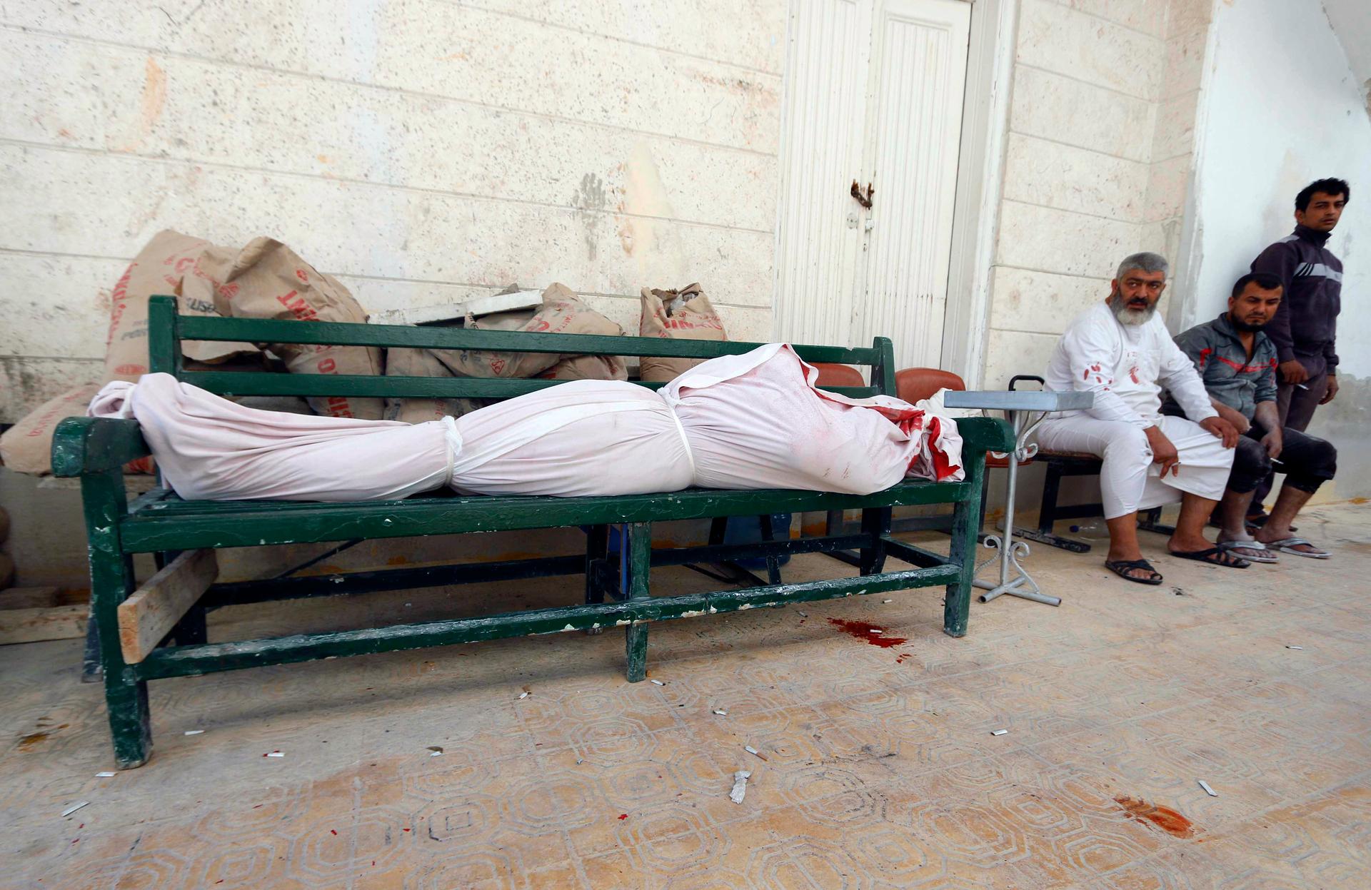 Men sit near a dead body wrapped in white after what activists said was a barrel bomb was dropped by forces loyal to Syrian President Bashar al-Assad in Aleppo on October 1, 2014. 