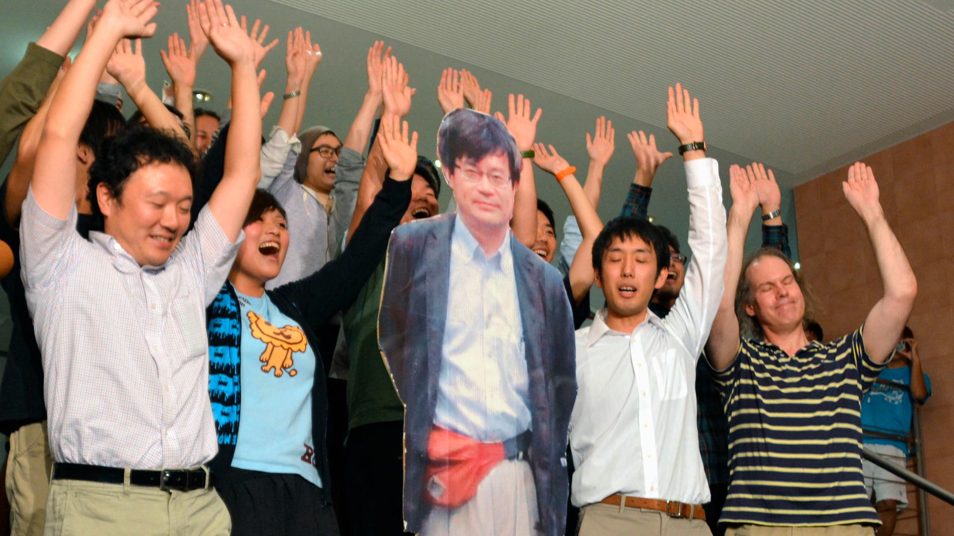 A life-size cardboard cutout photo of Japanese scientist Hiroshi Amano, a professor at Nagoya University, is surrounded by his laboratory staff members as they raise hands and shout "Banzai", or "Cheers."