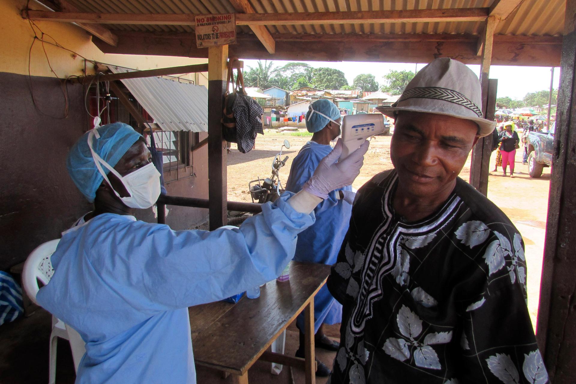 A health worker checks the temperature of a man at a roadside medical checkpoint outside Ganta, Liberia.