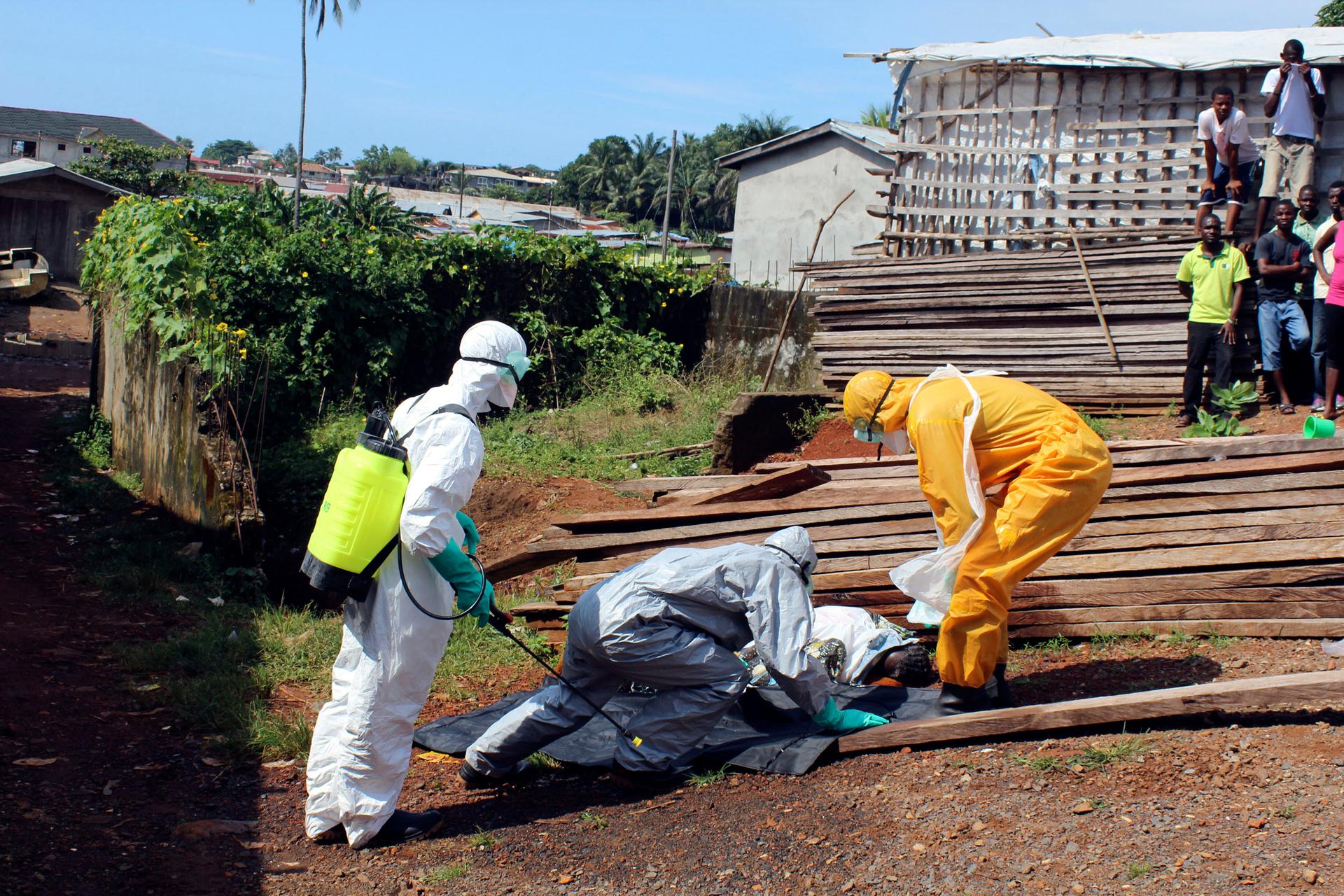 Health workers remove the body a woman who died from the Ebola virus in the Aberdeen district of Freetown, Sierra Leone, on October 14, 2014.