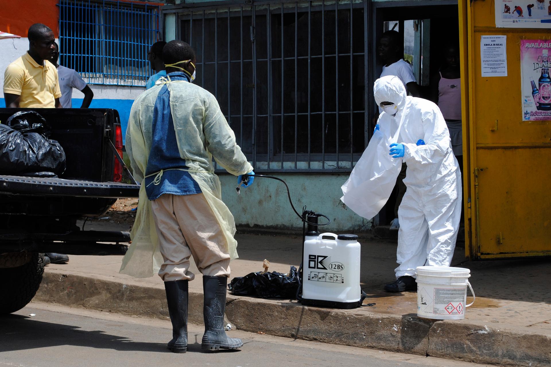 A member of a burial team prepares to spray a colleague with chlorine disinfectant in Monrovia.