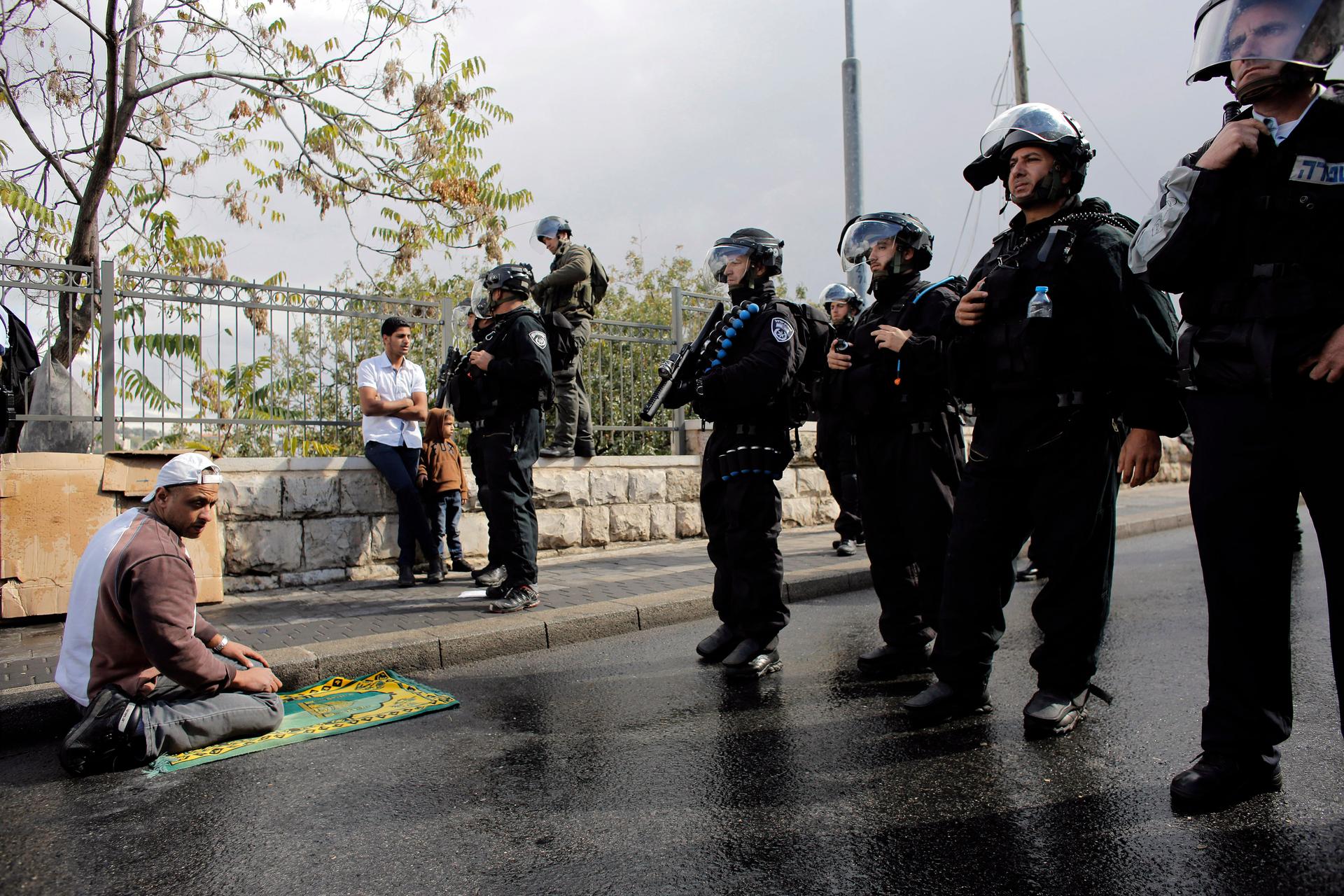 A Palestinian man prays near Israeli police during Friday prayers in the East Jerusalem neighbourhood of Wadi al-Joz on October 31, 2014. Israeli police declared an age limit on Friday for Palestinians wanting to enter the Old City, only allowing males ab