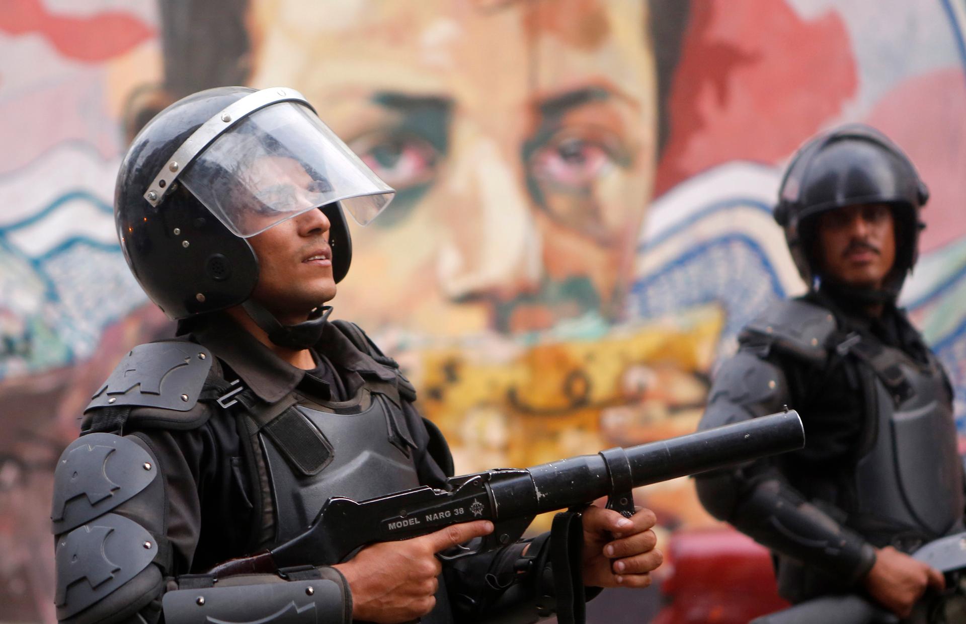Riot police walk along Mohamed Mahmoud Street, near Cairo's Tahrir Square, in front of murals representing people killed during Egypt's uprising.
