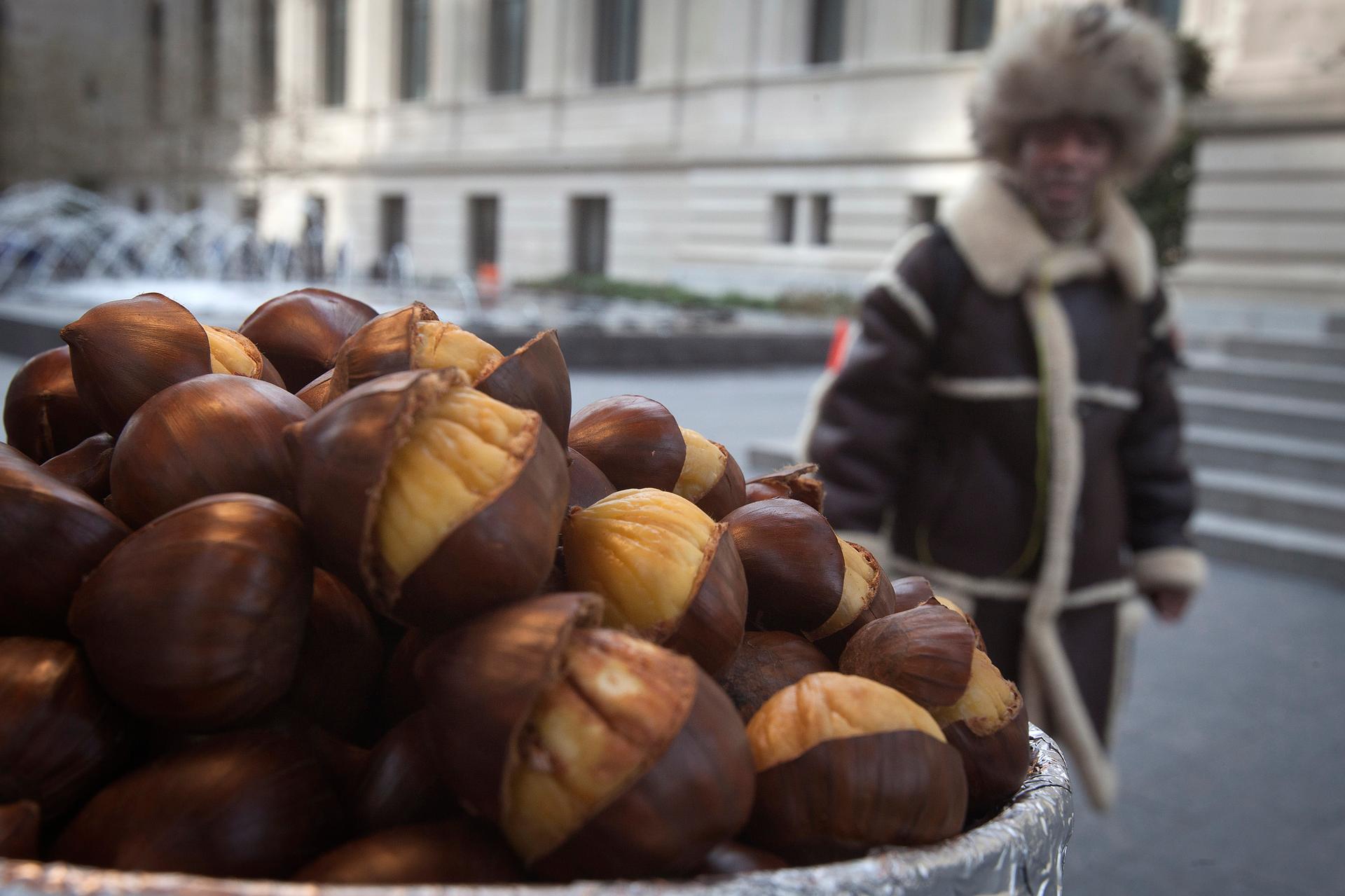 A man, bundled up against the cold, walks past a street vendor's chestnuts as they roast in front of the Metropolitan Museum of Art in New York.