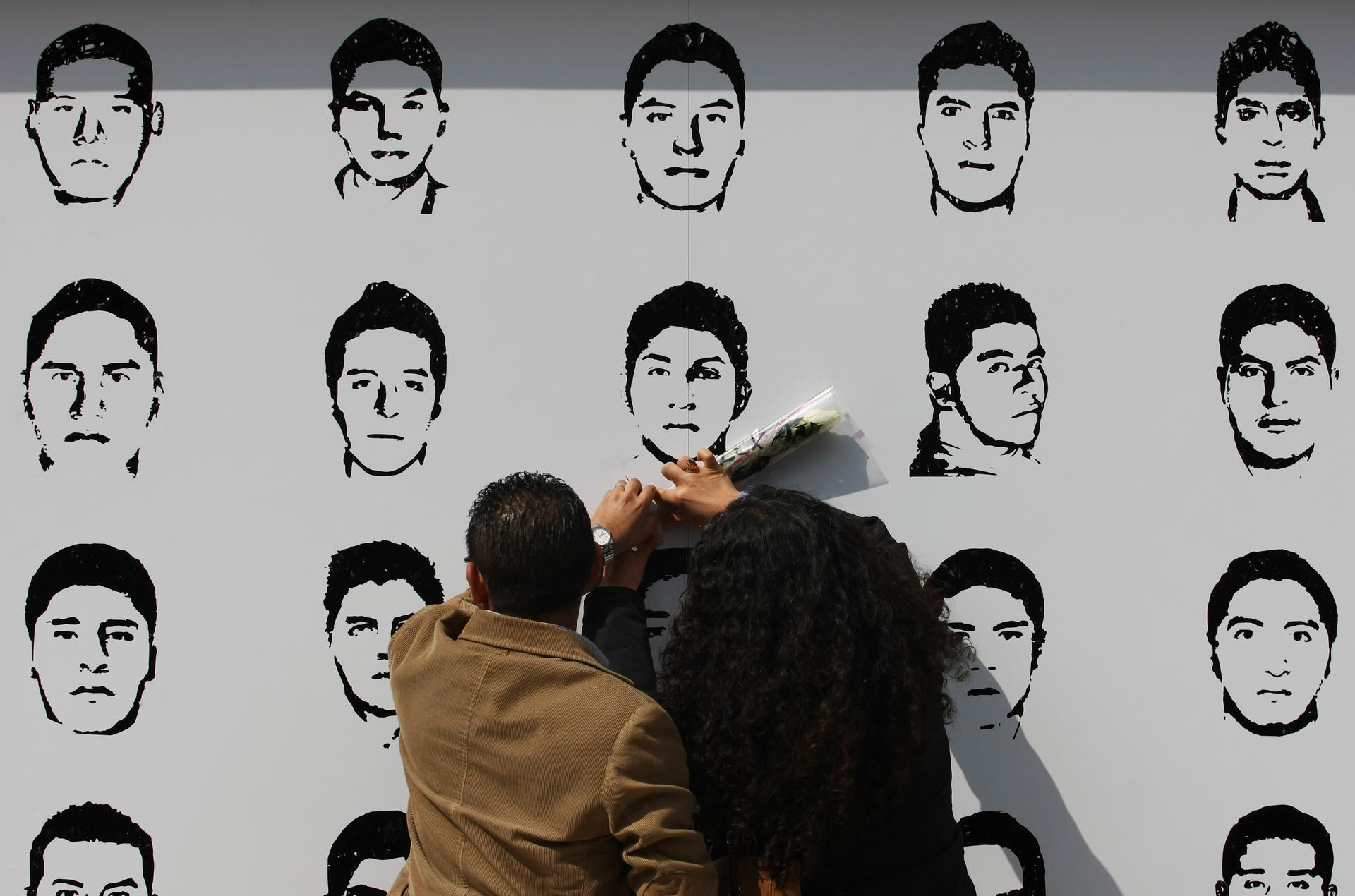 In Mexico City, people attach flowers to a mural showing the faces of the 43 missing trainee teachers from he Ayotzinapa Teacher Training College Raul Isidro Burgos.