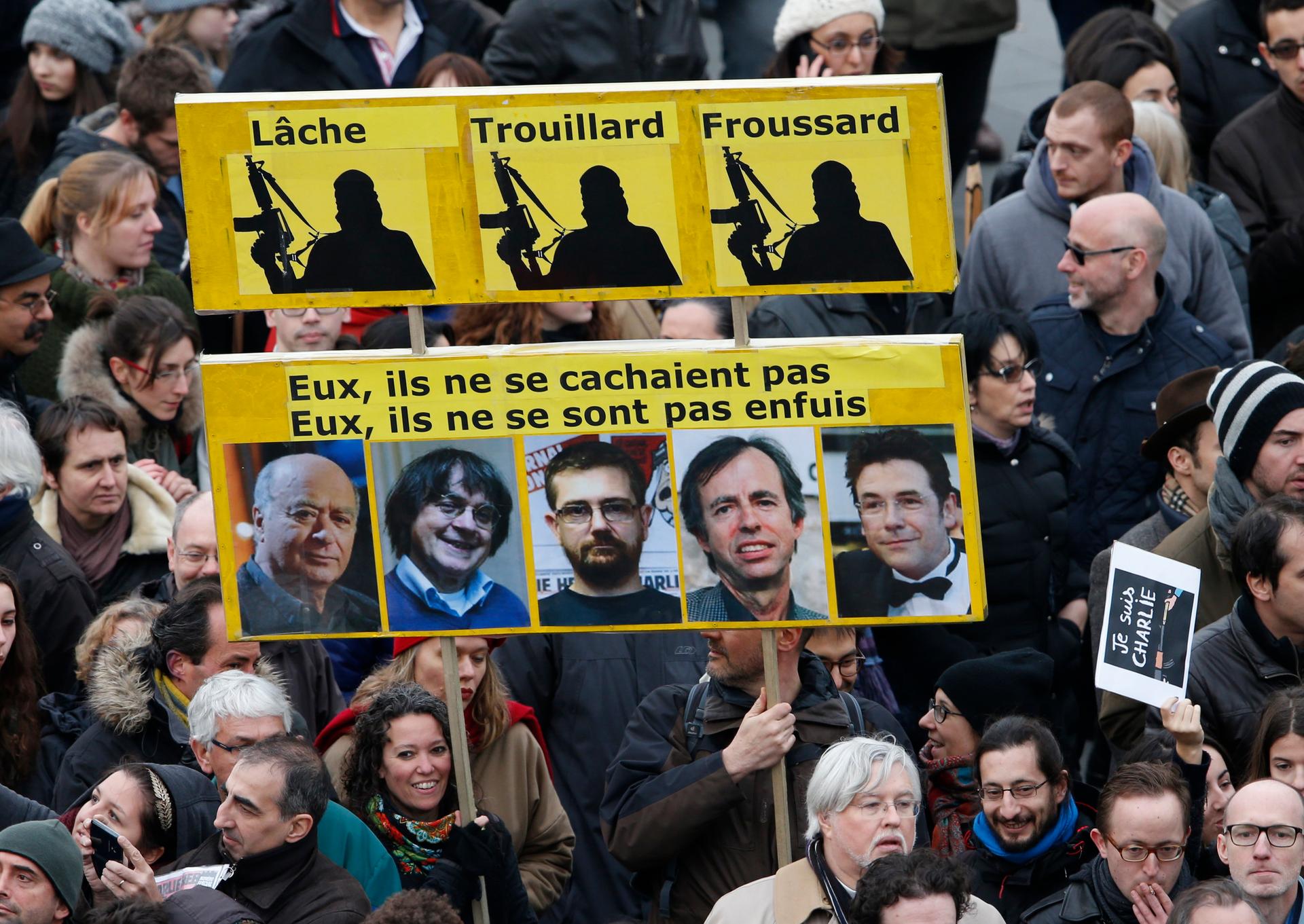 Citizens carrying a placard reading "Coward, Chicken, Yellow-Belly (top) and They, didn't hide. They they did not run (Bottom)" take part in a Hundreds of thousands of French citizens solidarity march (Marche Republicaine) in the streets of Paris January 