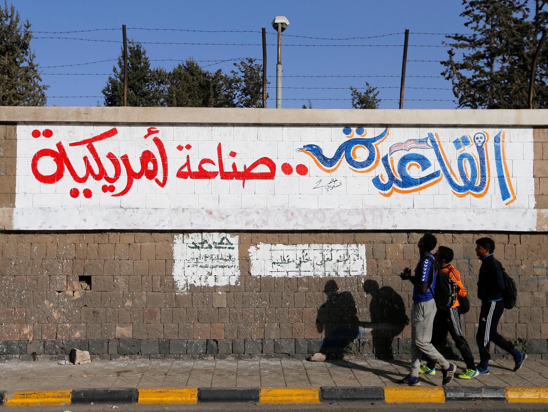 People walk past a graffiti reading "Al Qaeda is American-made"