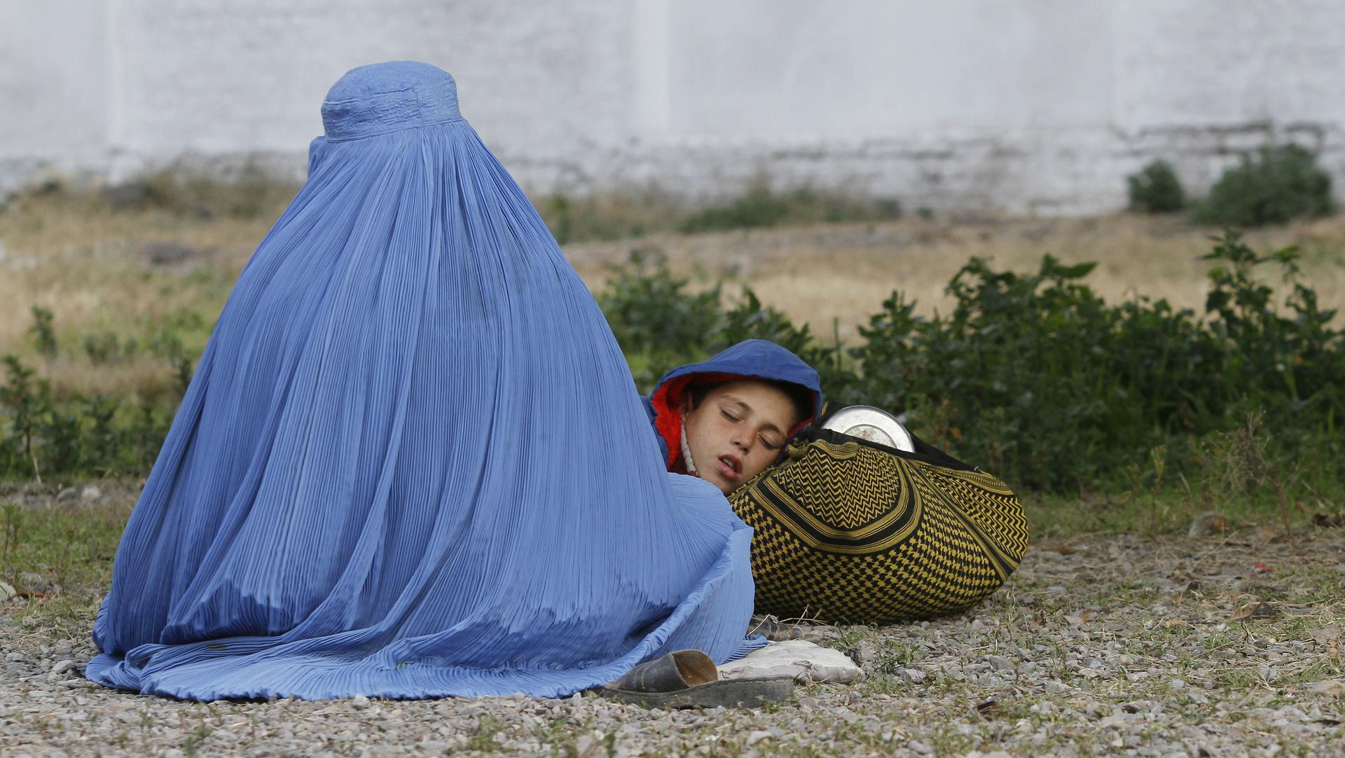 An Afghan refugee woman sits with her sleeping child as they wait with others to be repatriated to Afghanistan, at the United Nations High Commissioner for Refugees office on the outskirts of Peshawar, Pakistan, Feb. 2, 2015.