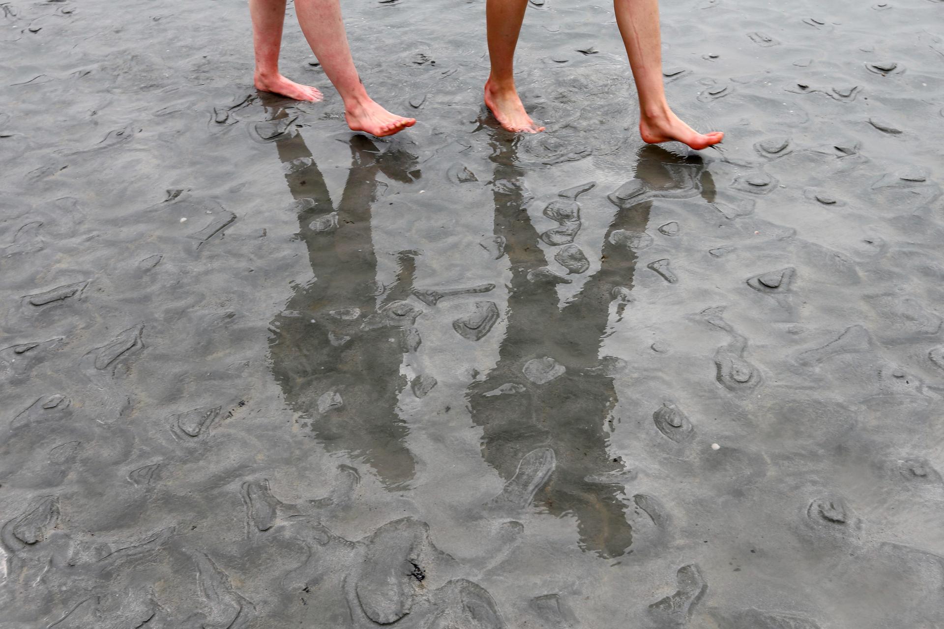 People cast shadows on the sand as they walk at low tide.