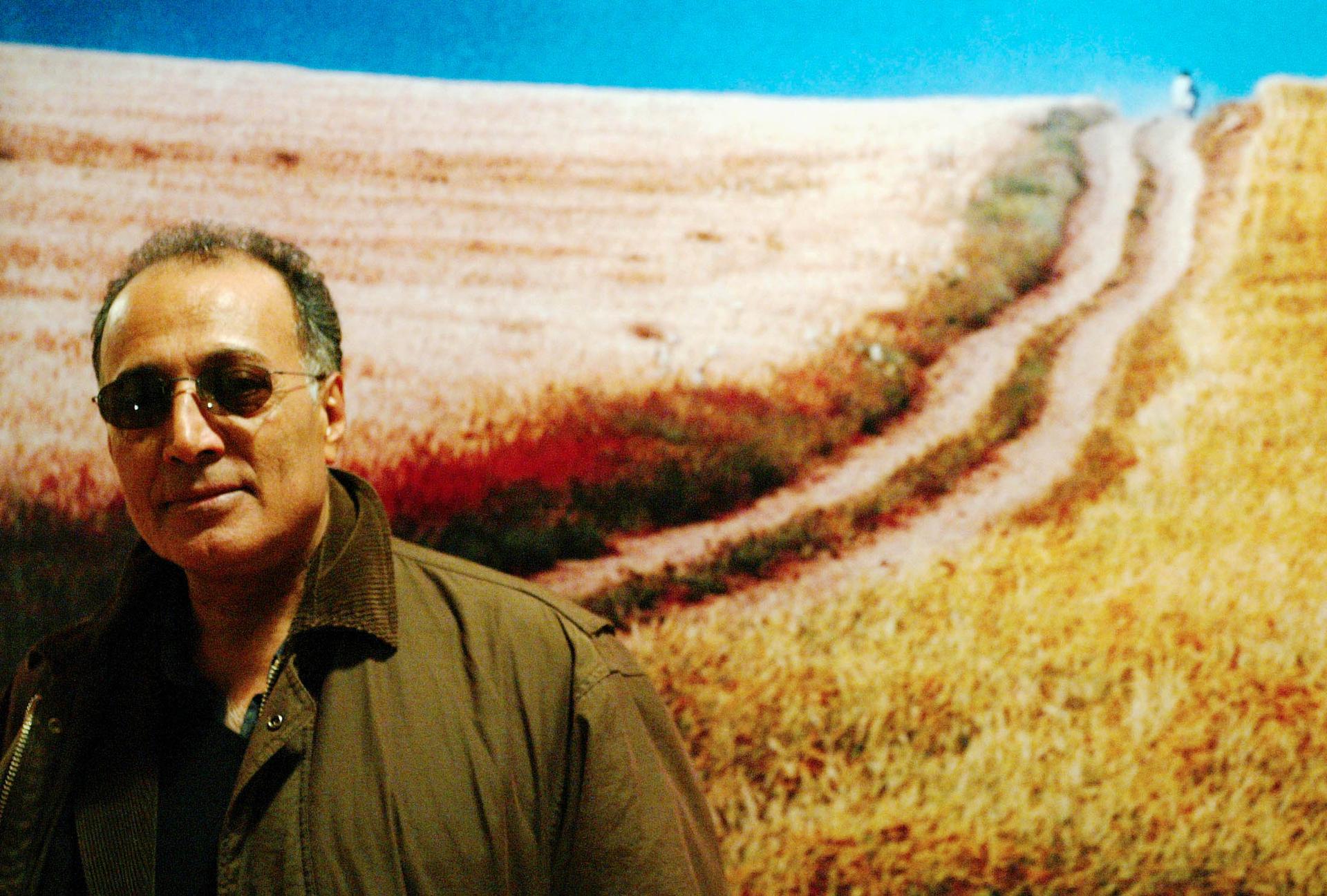 Iranian film director Abbas Kiarostami poses in front of a poster for his film "The Wind Will Carry Us" at the Portuguese film museum in Lisbon February 27, 2004.