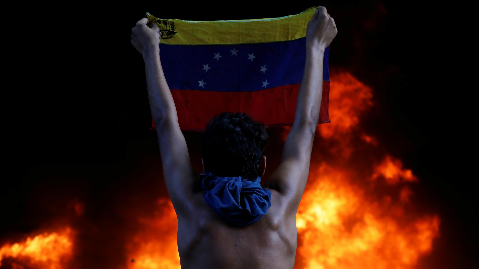 A protester holds a national flag as a bank branch, housed in the Supreme Court of Justice, burns during a rally against Venezuela's President Nicolás Maduro, in Caracas, Venezuela, June 12, 2017. 