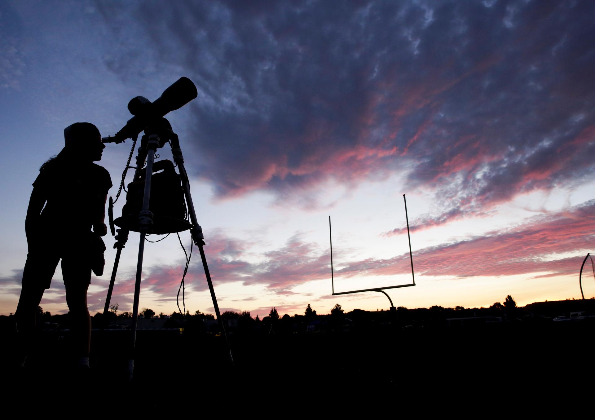 A woman looks through a telescope on the football field at Madras High School the evening before a solar eclipse in Madras, Oregon, Aug. 20, 2017.