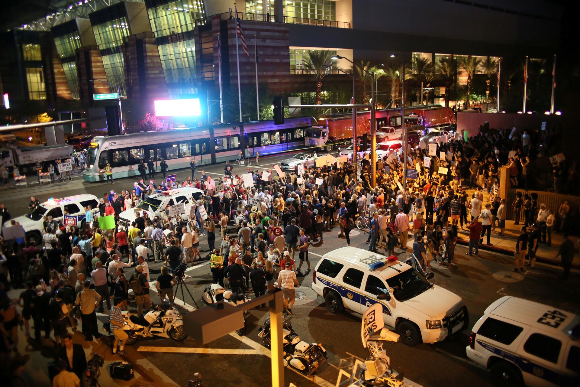 Overhead shot of crowd flanked by police SUVs, evening time