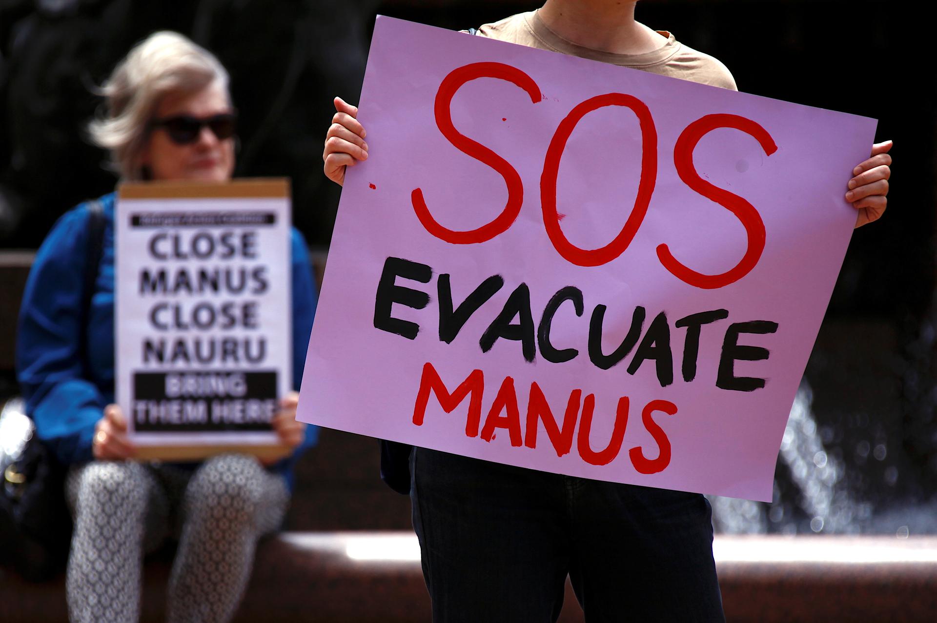A pink sign reading "SOS EVACUATE MANUS" is held up by a protester.