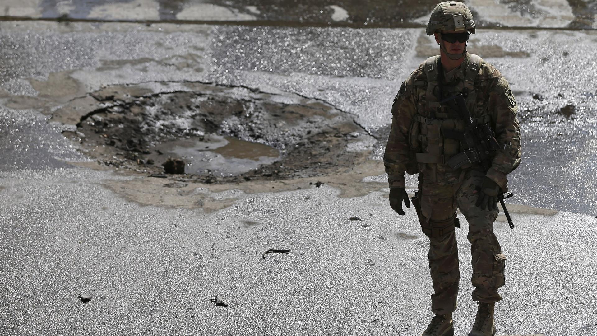 A NATO soldier stands at the site of a suicide car bomb blast in Kabul, on October 11th.  A suicide car bomber targeted a convoy of foreign troops in the Afghan capital during rush hour-traffic, flipping an armored vehicle on its side.  No fatalities were