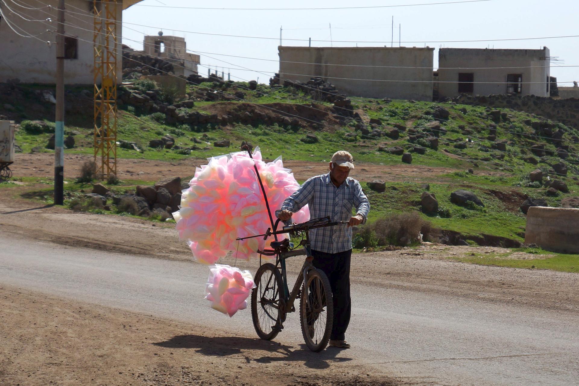A man sells cotton candy as he pushes his bicycle along a street in the rebel held al-Ghariyah al-Gharbiyah town, in Deraa province.