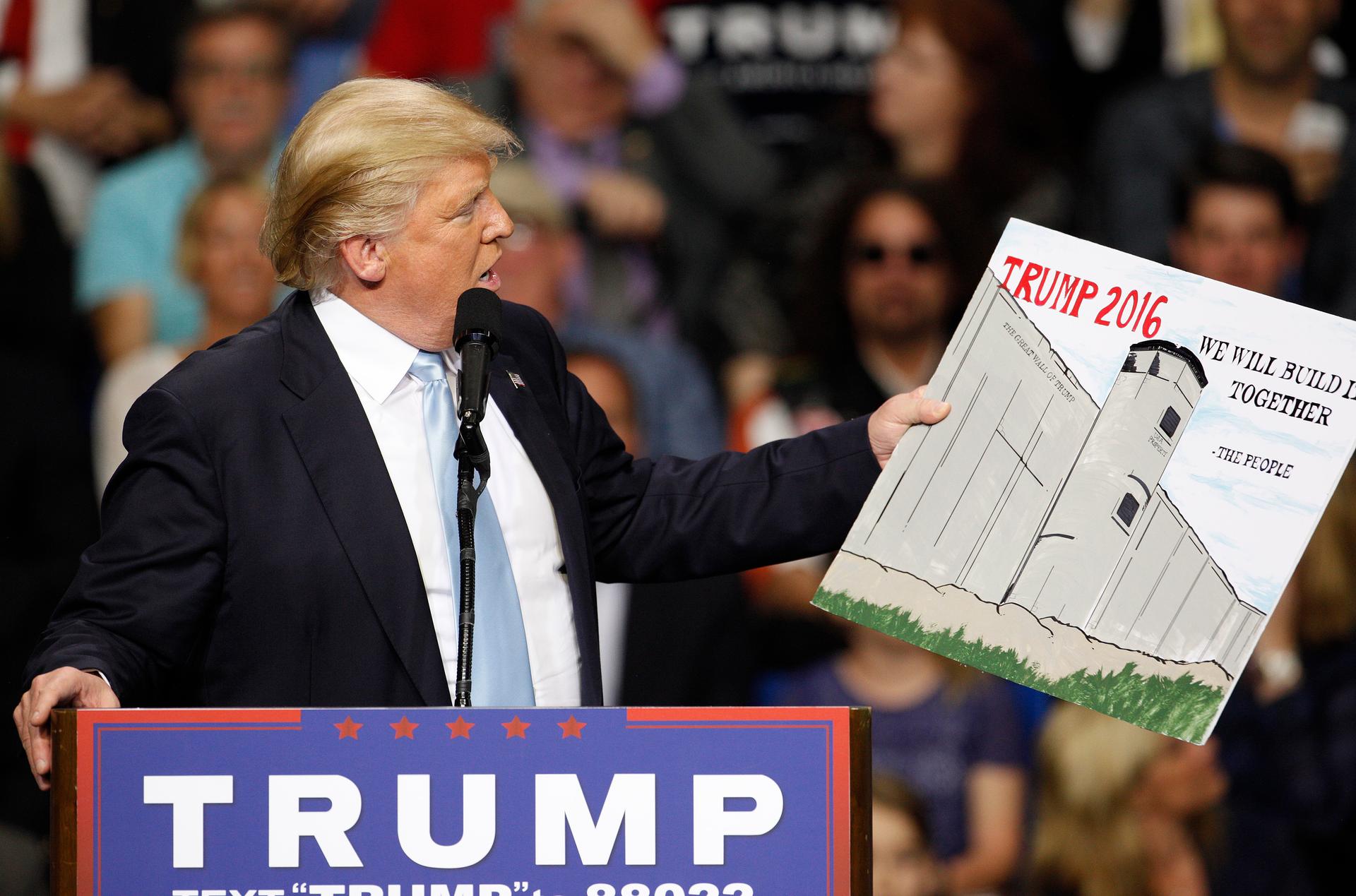 Donald Trump holds a sign supporting his plan to build a wall