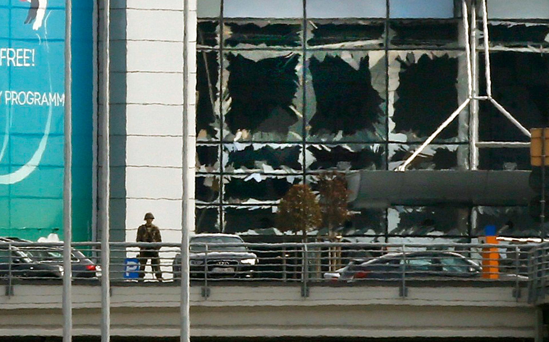 A soldier stands near broken windows after explosions at Zaventem airport near Brussels